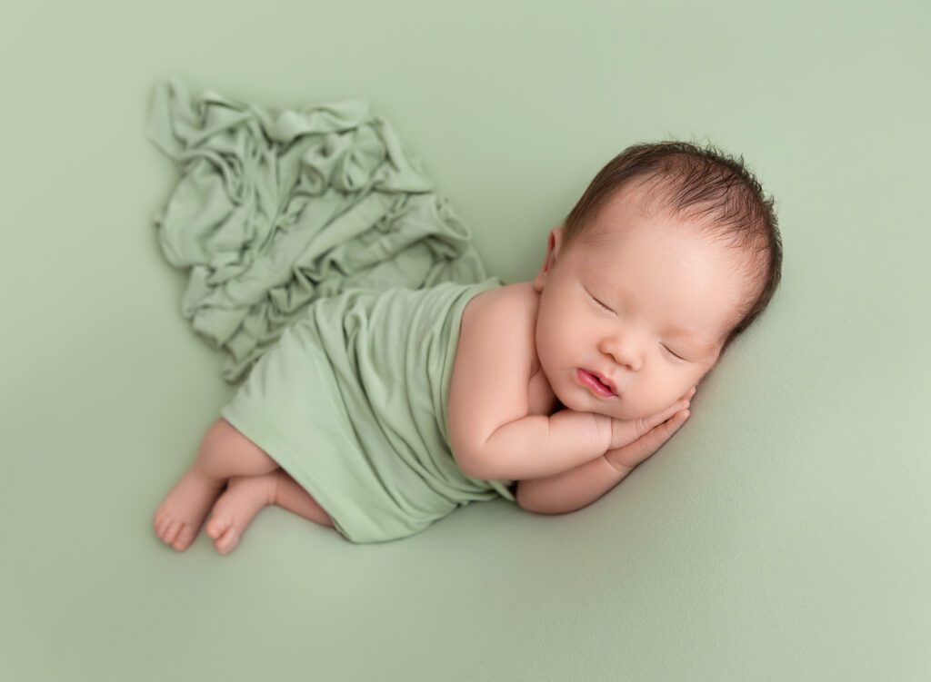 Sleeping Asian American baby wrapped in sage green wrap Brooklyn Ny