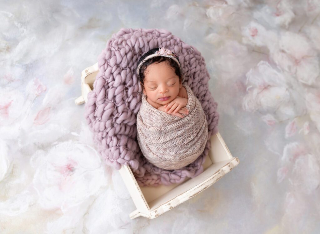 Newborn baby asleep in miniature crib with lilac wrap