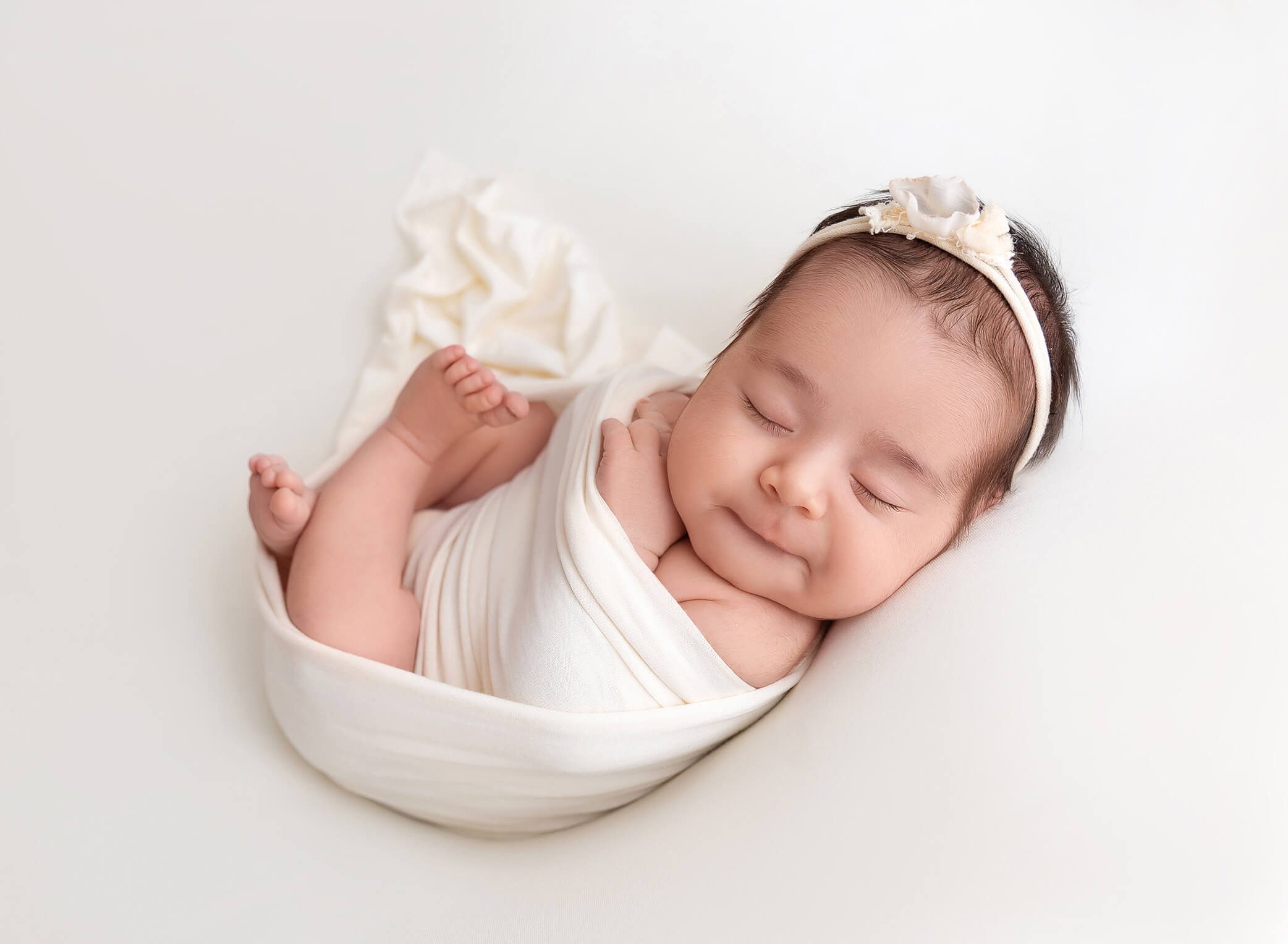 Newborn baby girl wrapped in cream wrap smiling at Rochel Konik photography studio