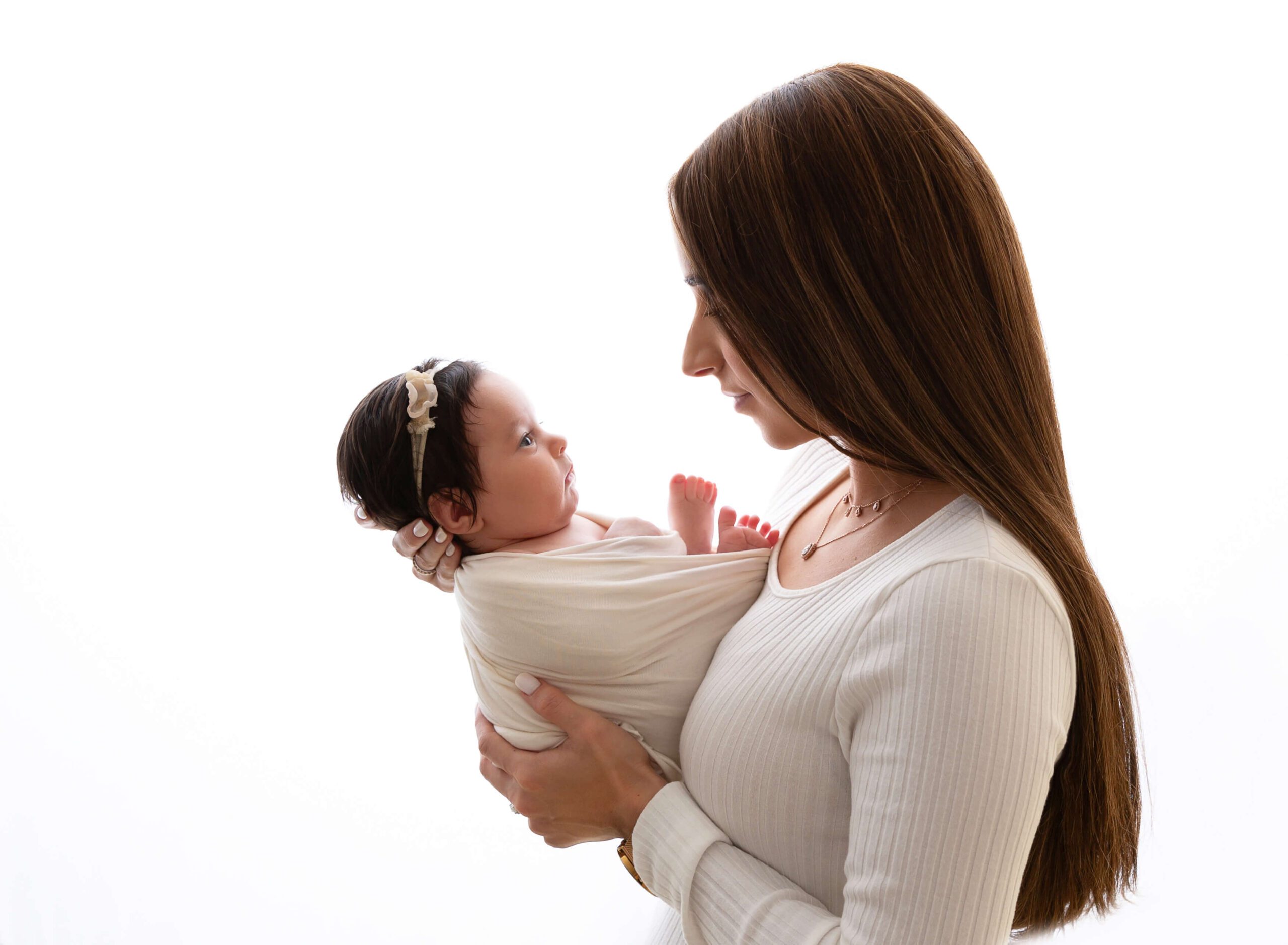 A newborn baby in a white swaddle looks up to mom while she holds her in a studio after leaving birthing centers in new york