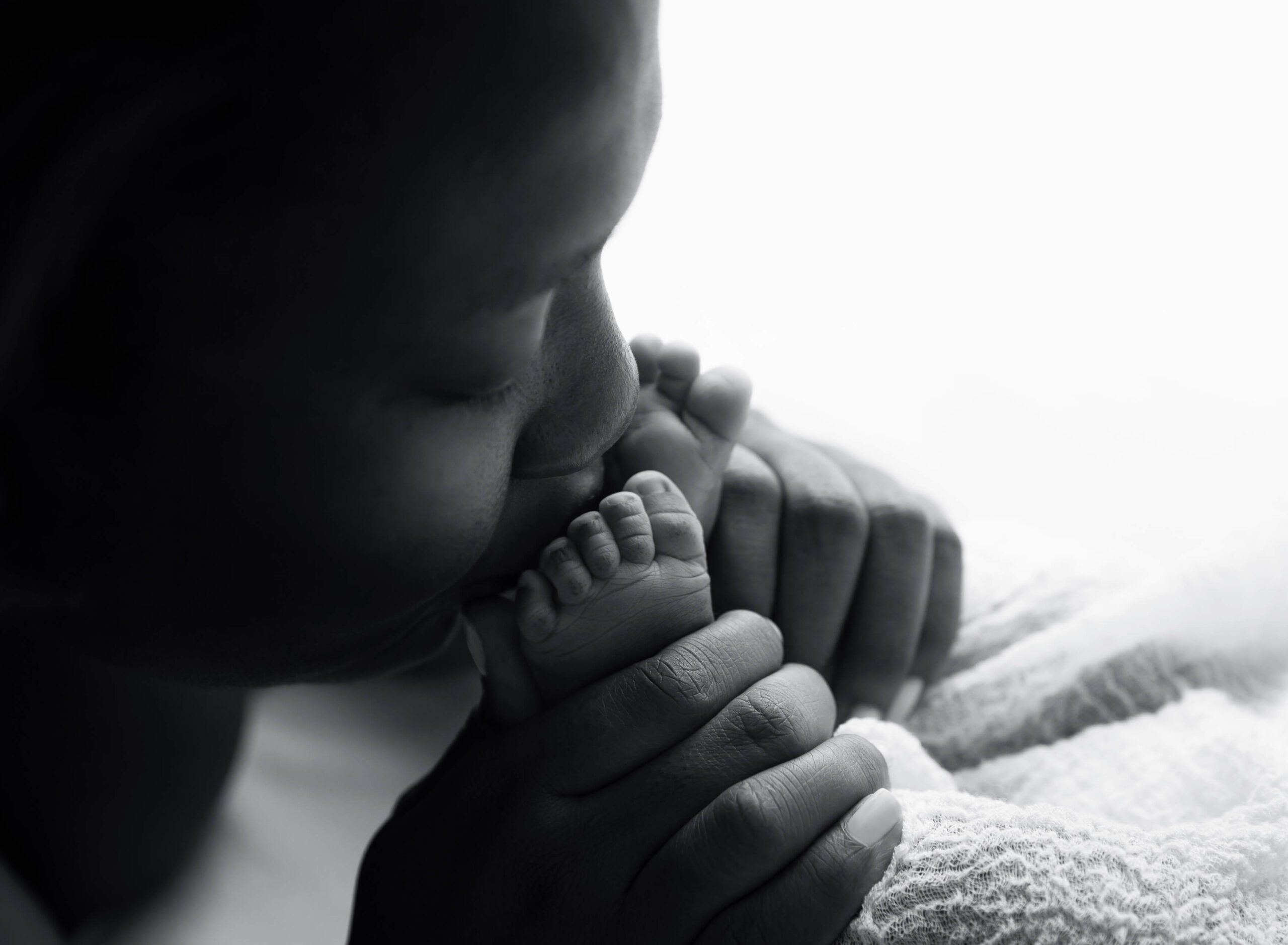 A new mom kisses the feet of her newborn baby in a studio on a bed