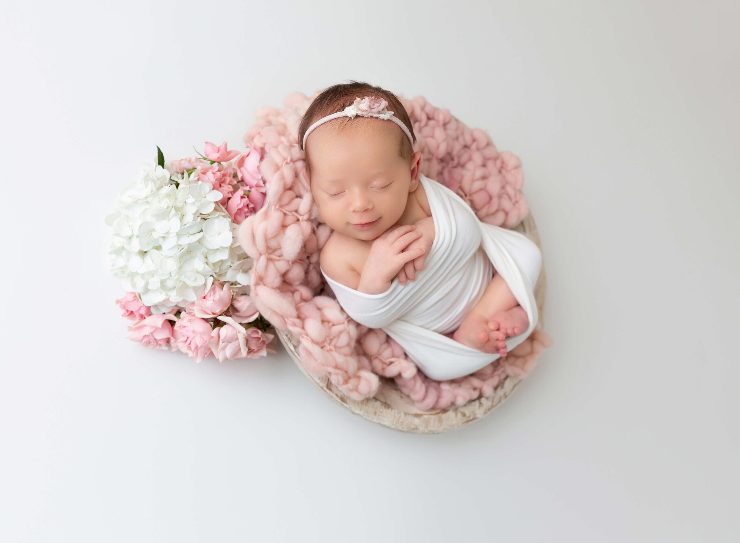 A sleeping newborn baby smiles in a basket and white open swaddle after meeting with brooklyn doulas