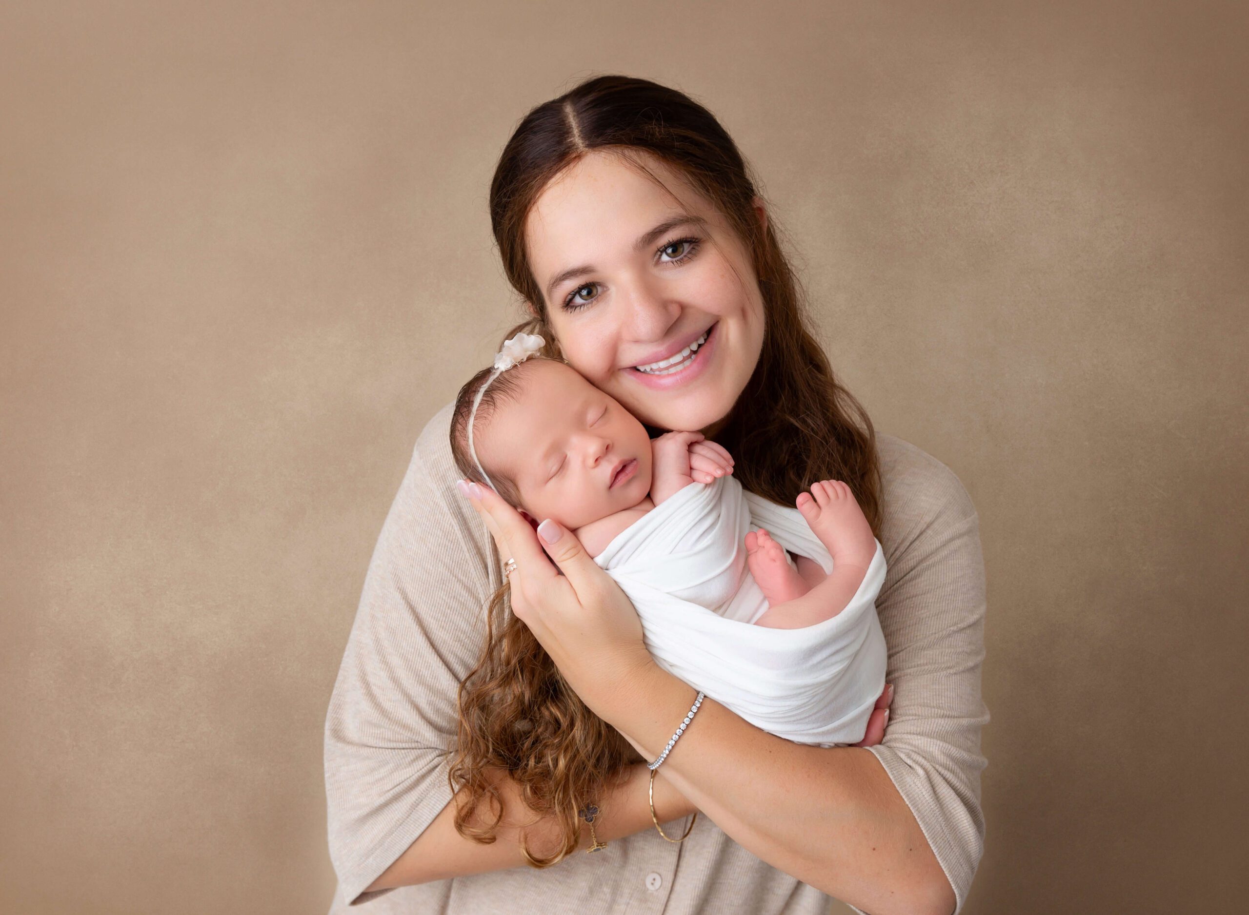 A newborn baby cuddles with mom while sleeping in her hands in a studio in a white swaddle after meeting brooklyn doulas