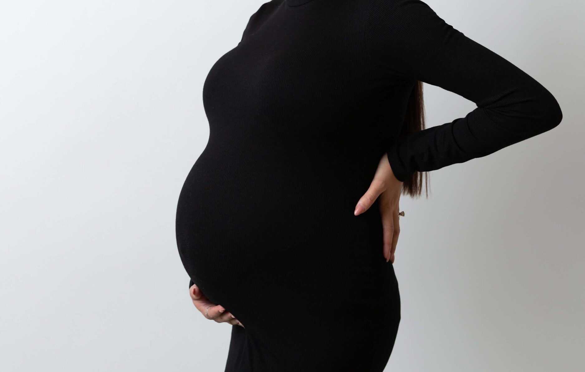 A happy mother to be in a black gown smiles while looking up and standing in a studio after meeting with Brooklyn midwives