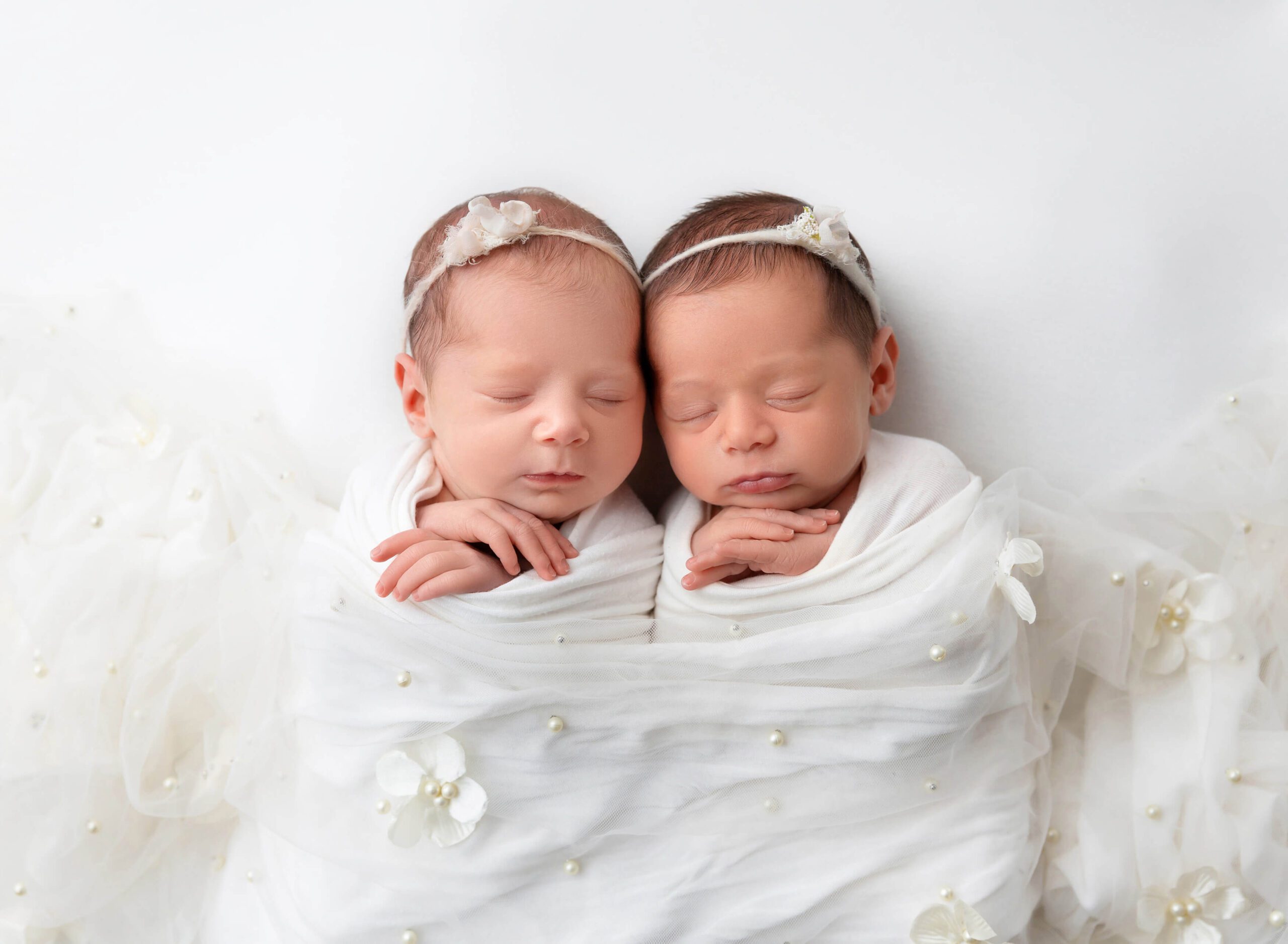 Sleeping newborn baby twin sisters in white swaddles in a studio