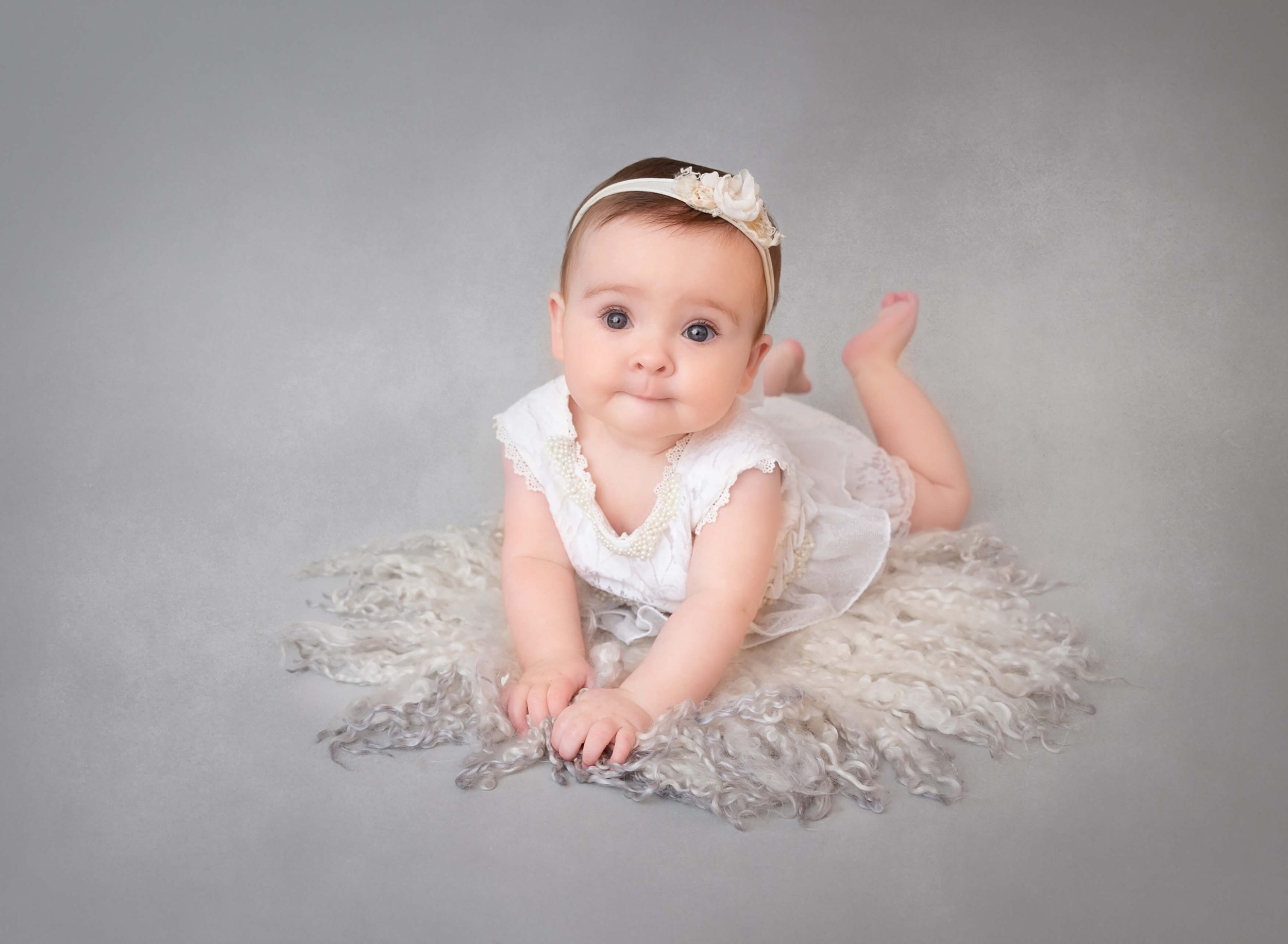 A baby crawls on a studio floor in a white dress and flower headband after meeting nannies in New York