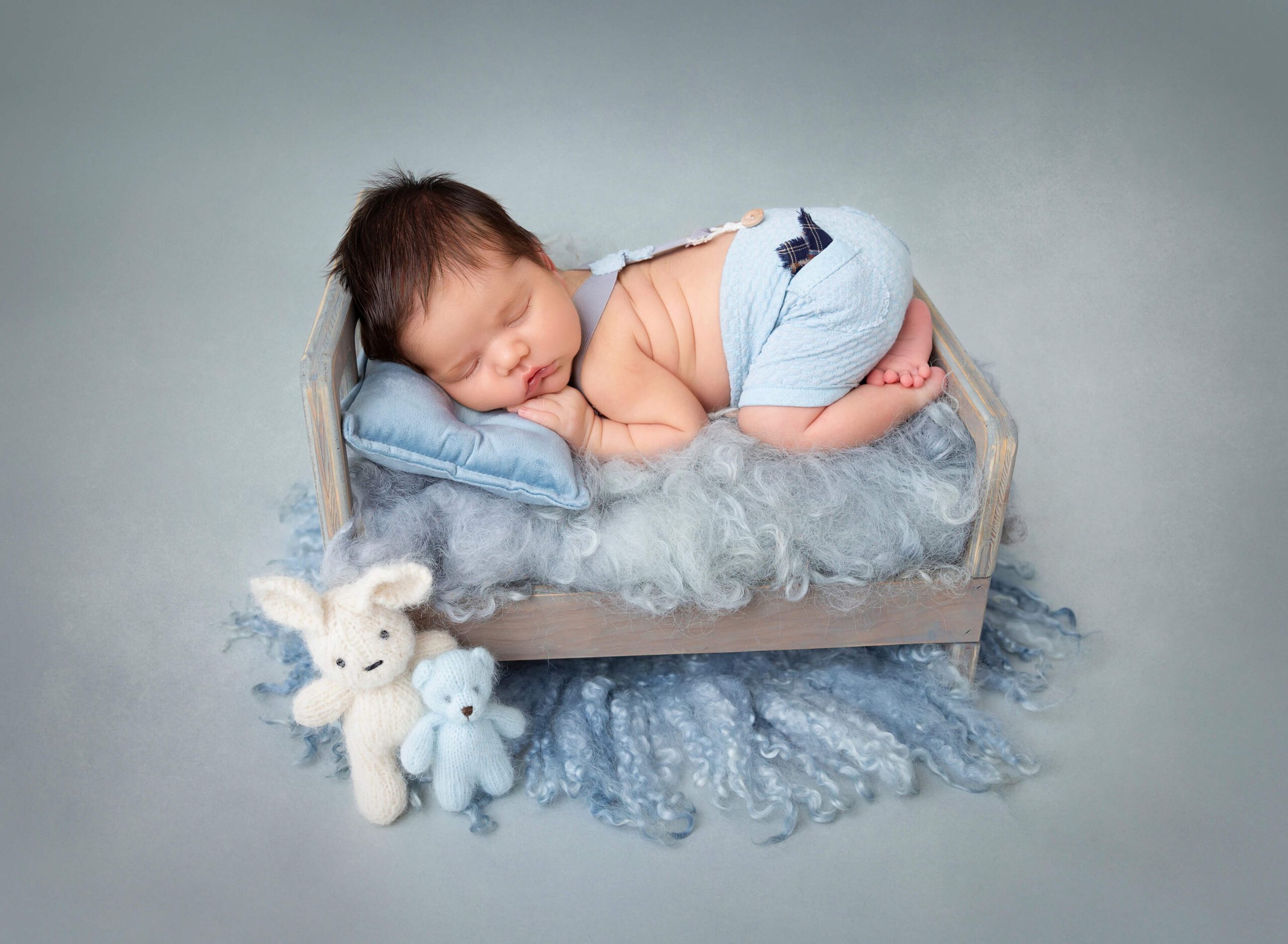 A newborn baby sleeps on its tummy in a tiny wooden bed with stuffed felt bears