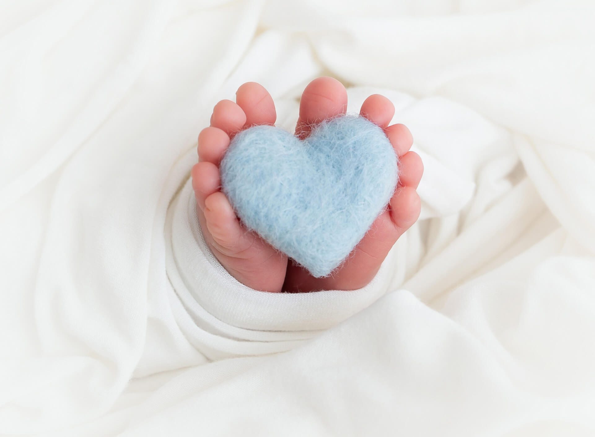 Details of a newborn baby's feet holding a tiny blue felt heart after using an obgyn new york