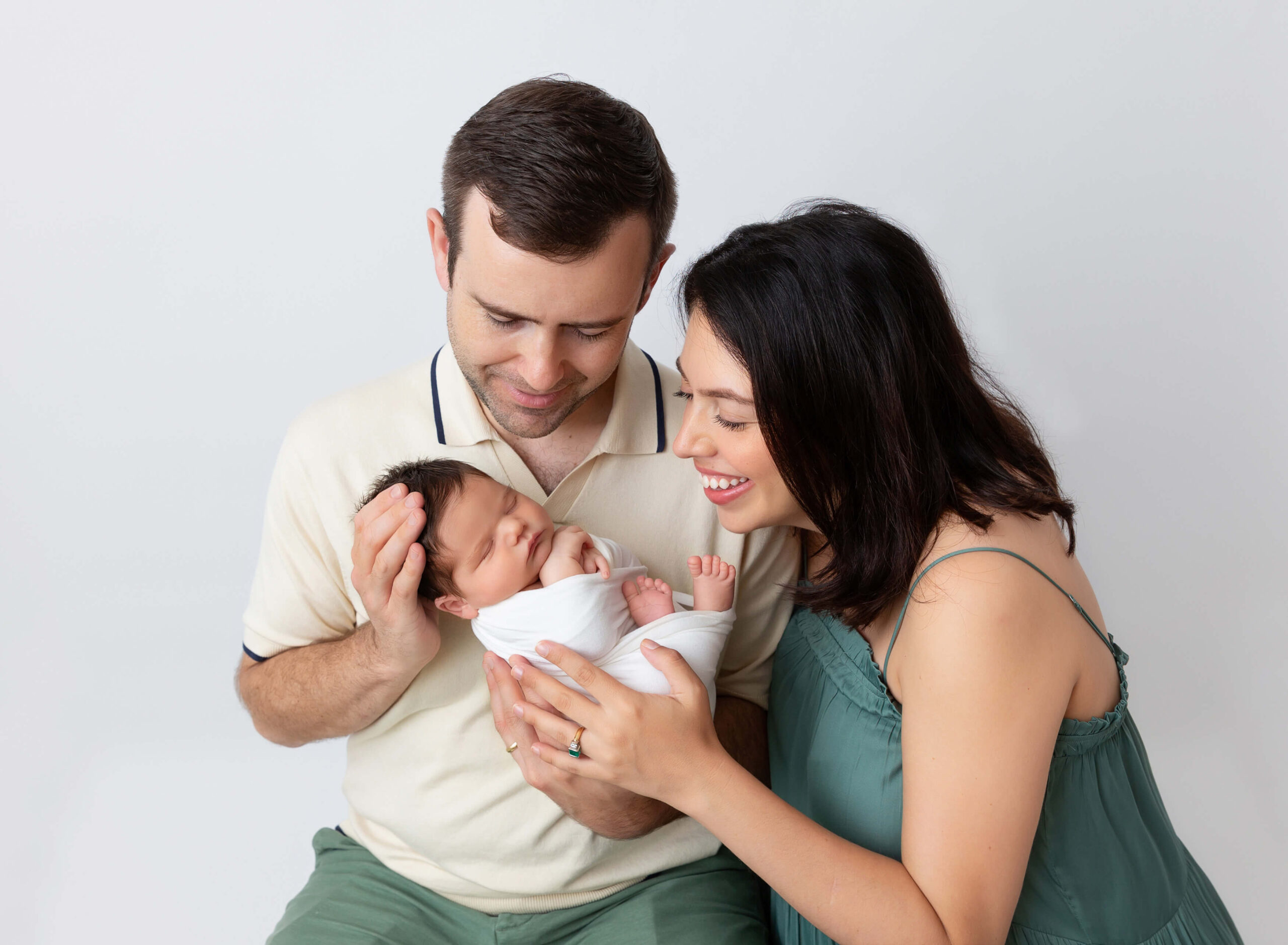 Happy new parents cradle their sleeping newborn baby in their hands while sitting in a studio thanks to an obgyn new york