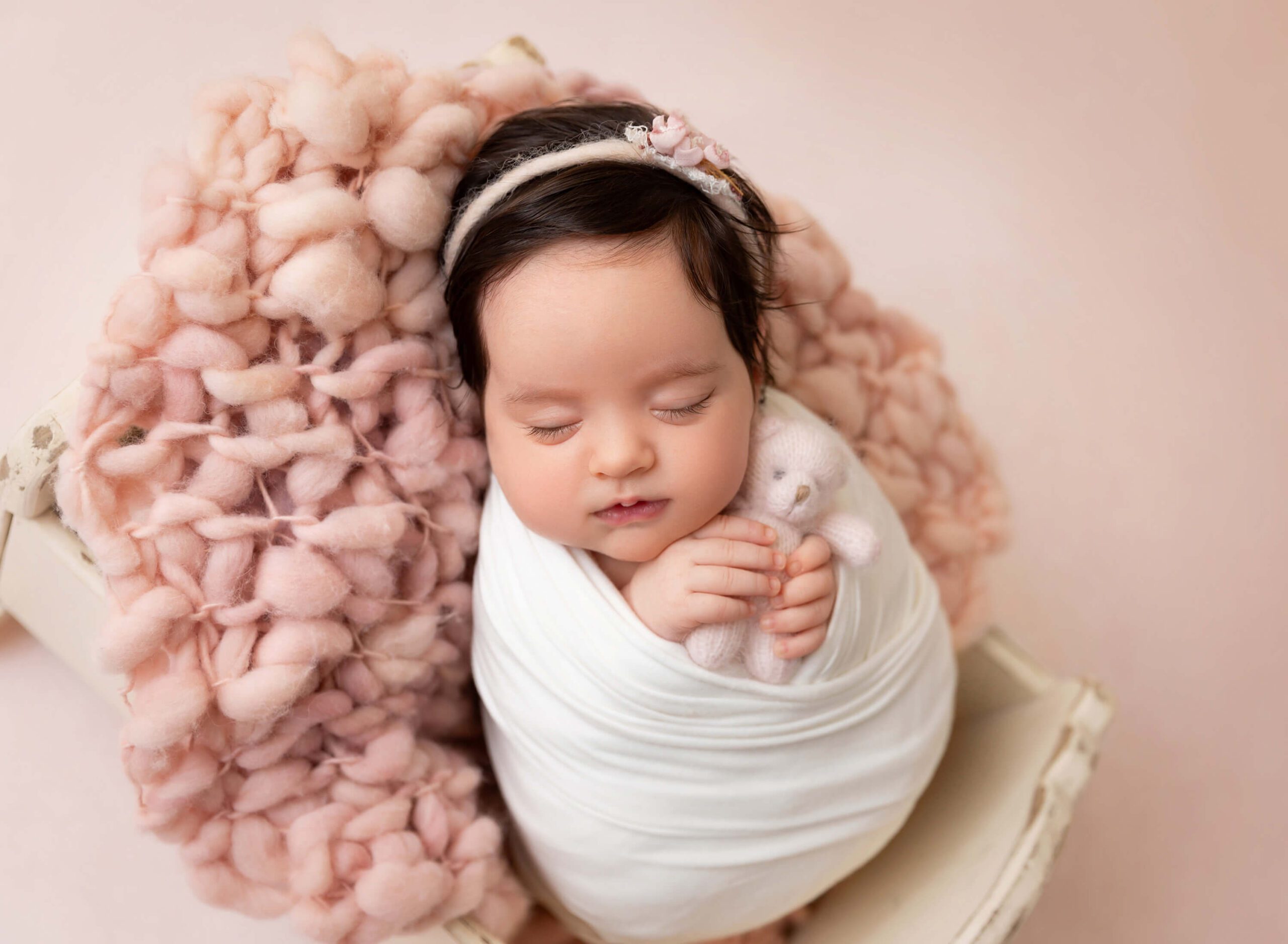 Baby girl wrapped in white and holding the pink bear in her tiny hands 