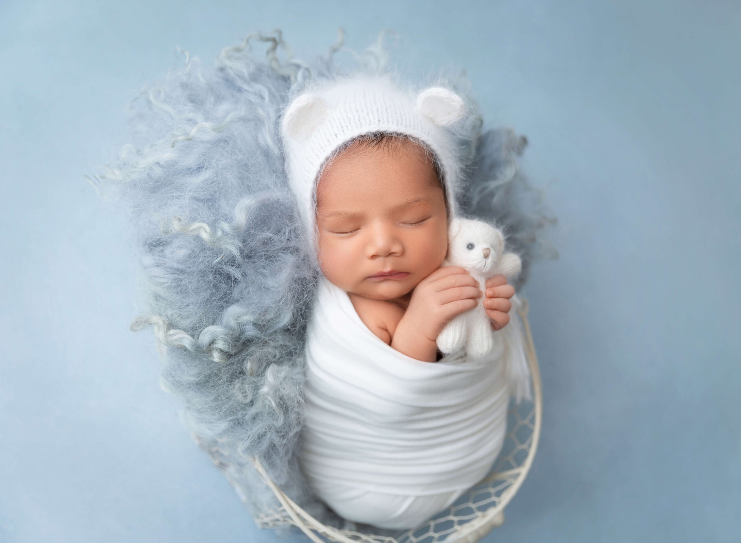 Newborn baby boy swaddled in white holding tiny teddy bear