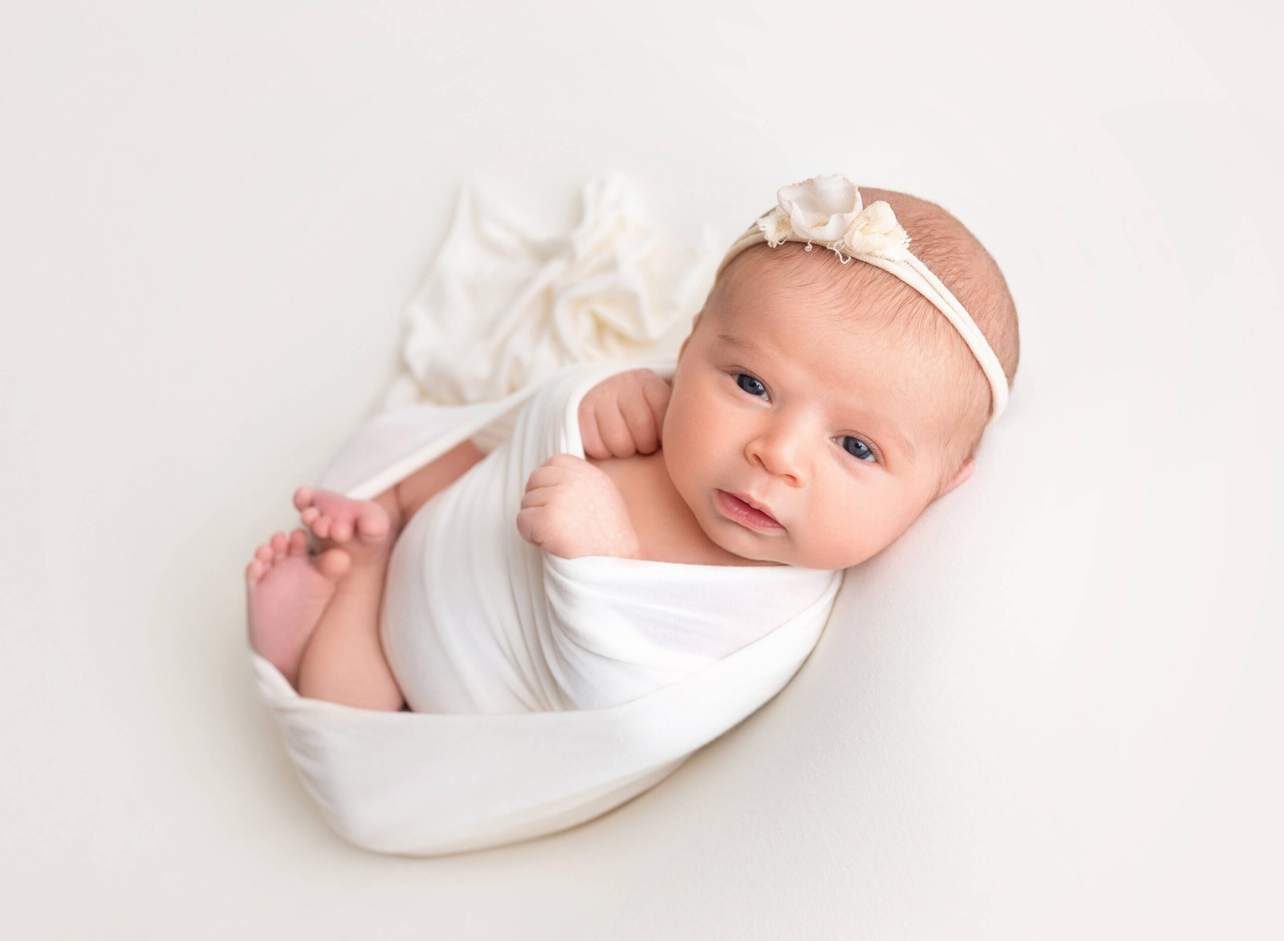 Awake Newborn baby girl wrapped in white in a studio after a prenatal massage in new york