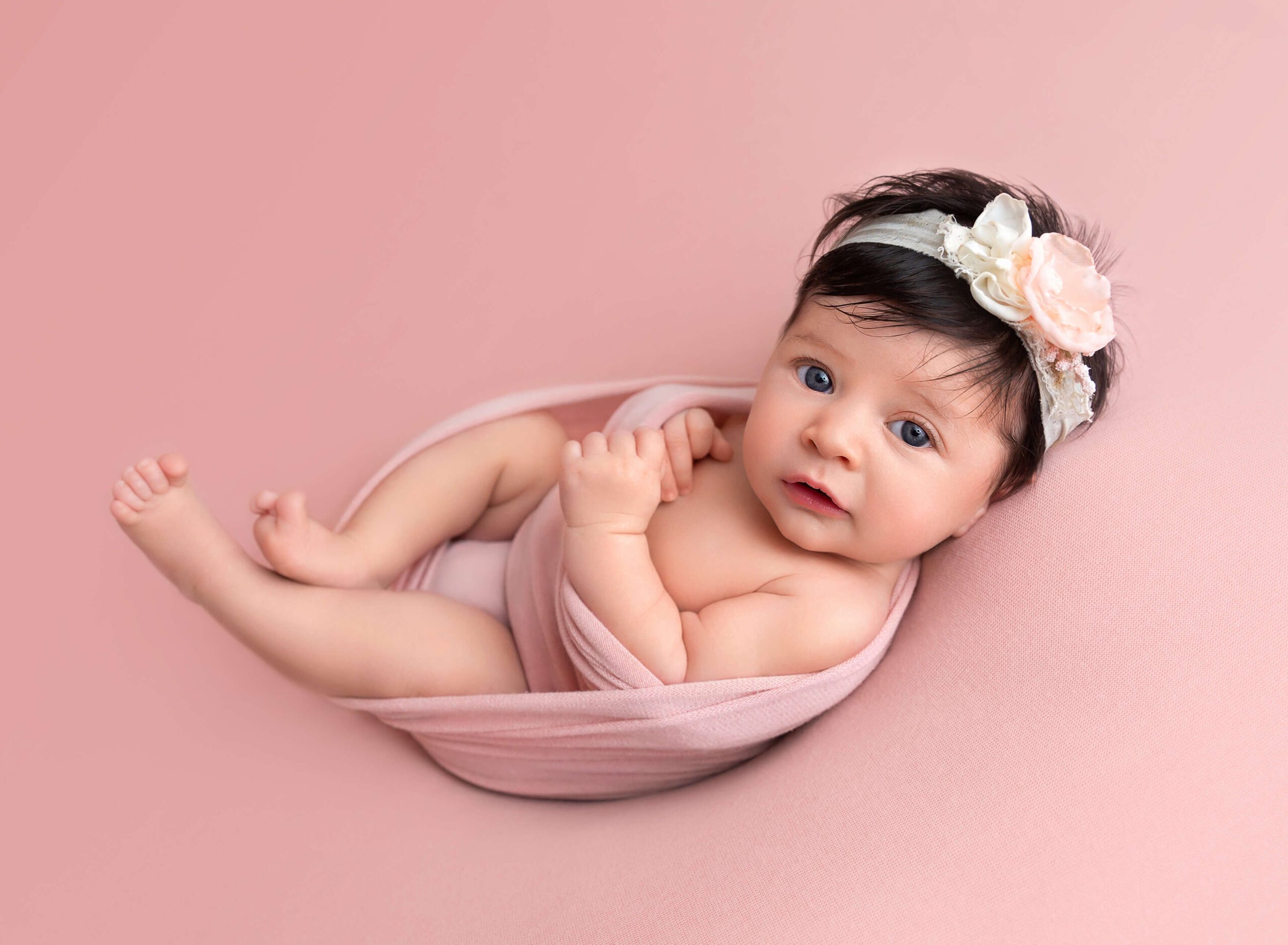 Awake Newborn baby girl wrapped in pink with a pink bow headband