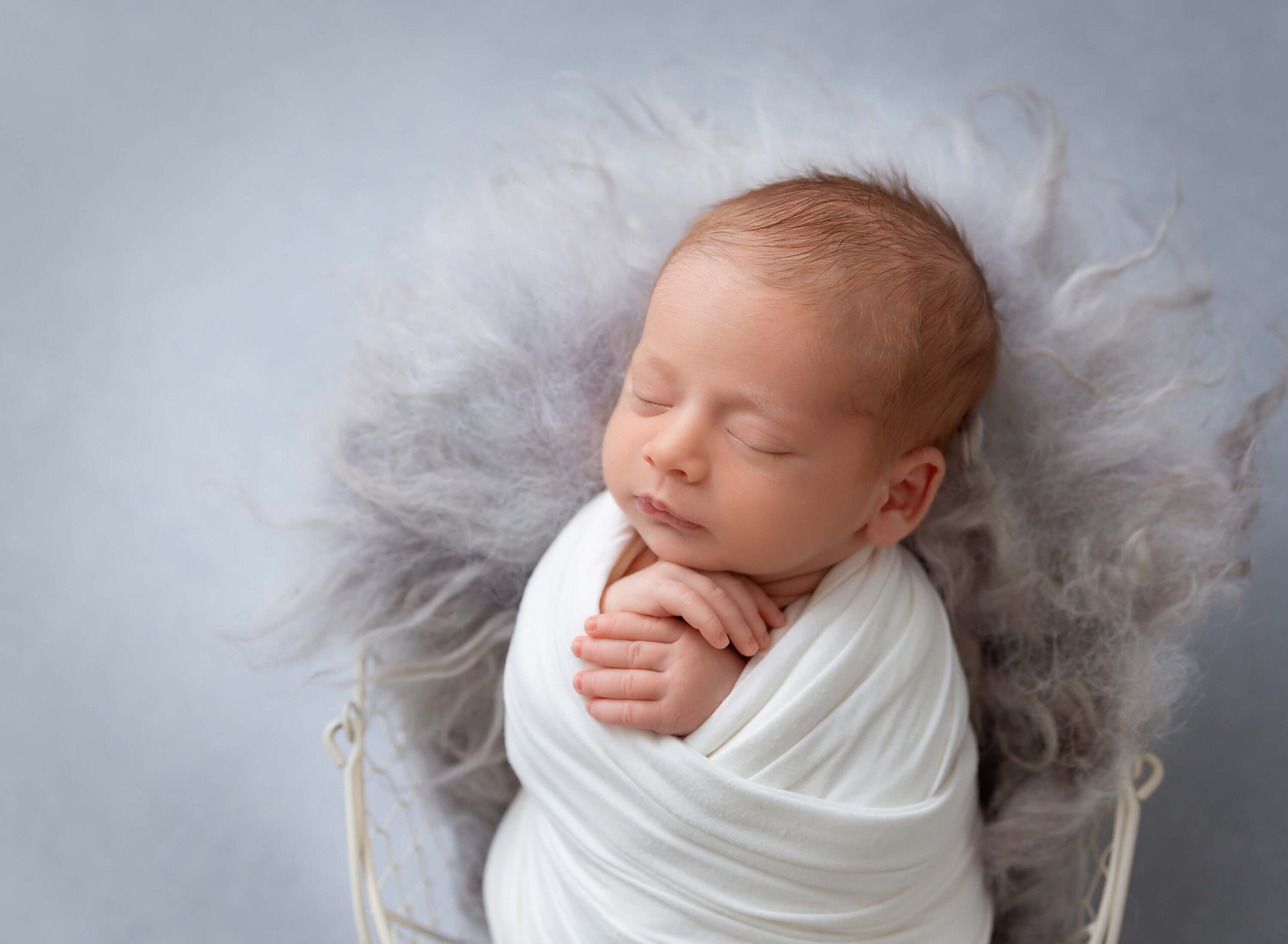 A sleeping newborn in a white swaddle with hands out in a tin bucket after an infant massage in nyc