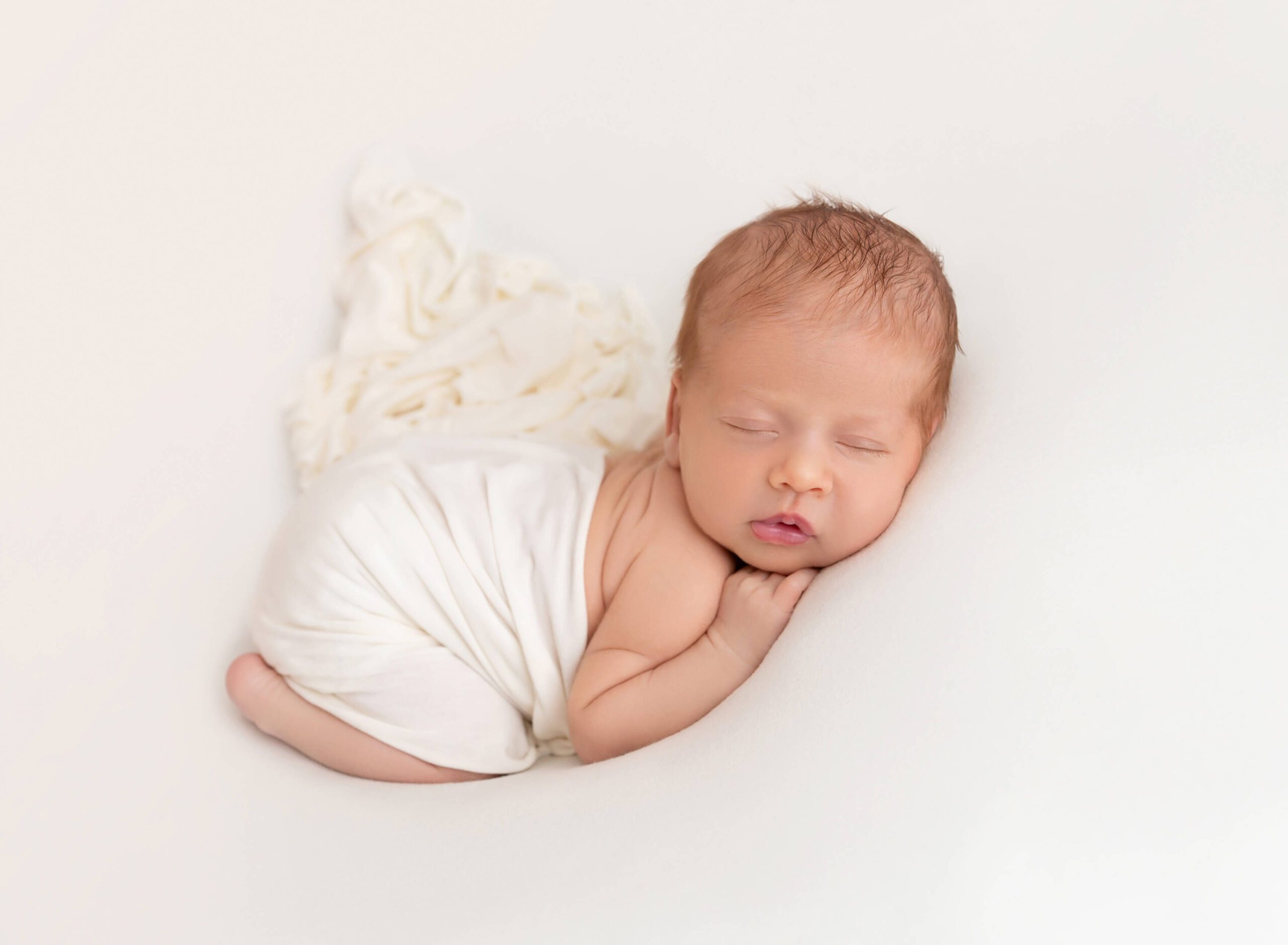 A newborn baby sleeps in froggy pose on a white bed in a studio after an infant massage in nyc