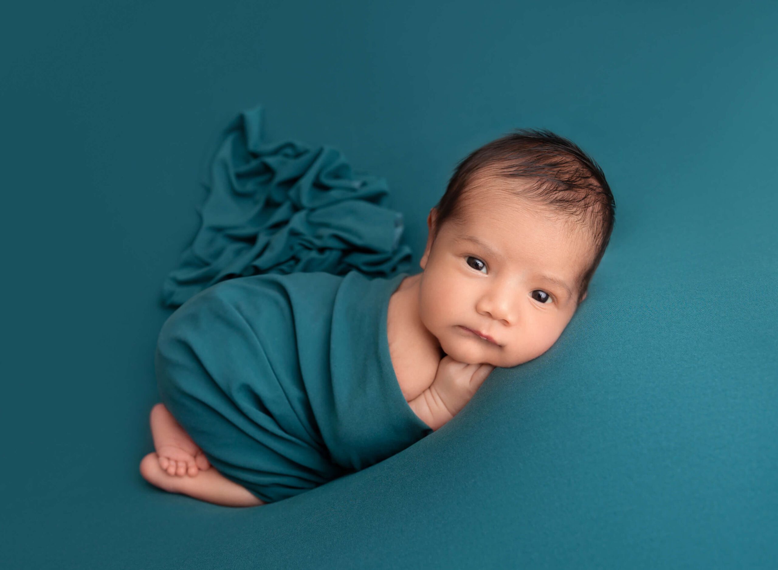 A newborn baby lays under a blue blanket with eyes open after visiting pediatric dentists in new york