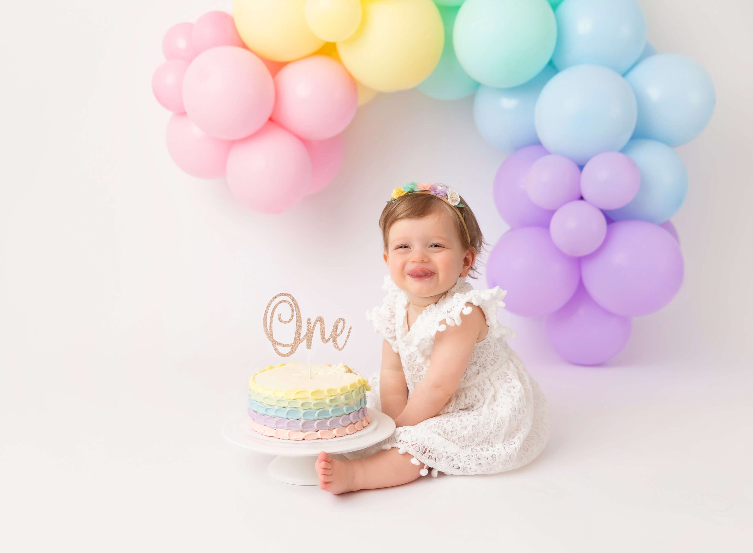 A baby sits in a studio with balloons smiling big behind a colorful cake after meeting pediatricians in new york