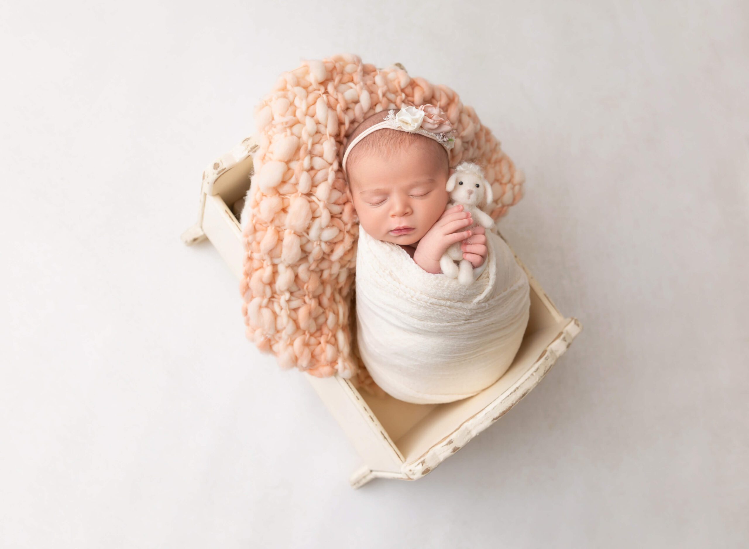 A newborn baby sleeps in a wooden crib holding a tiny stuffed bunny after mom had a prenatal massage in new york