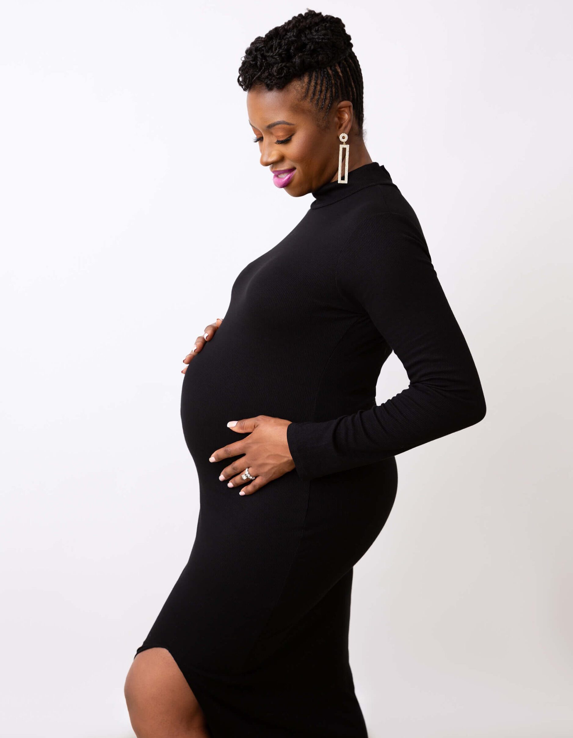 A pregnant woman smiles down at her hands on her bump in a black gown