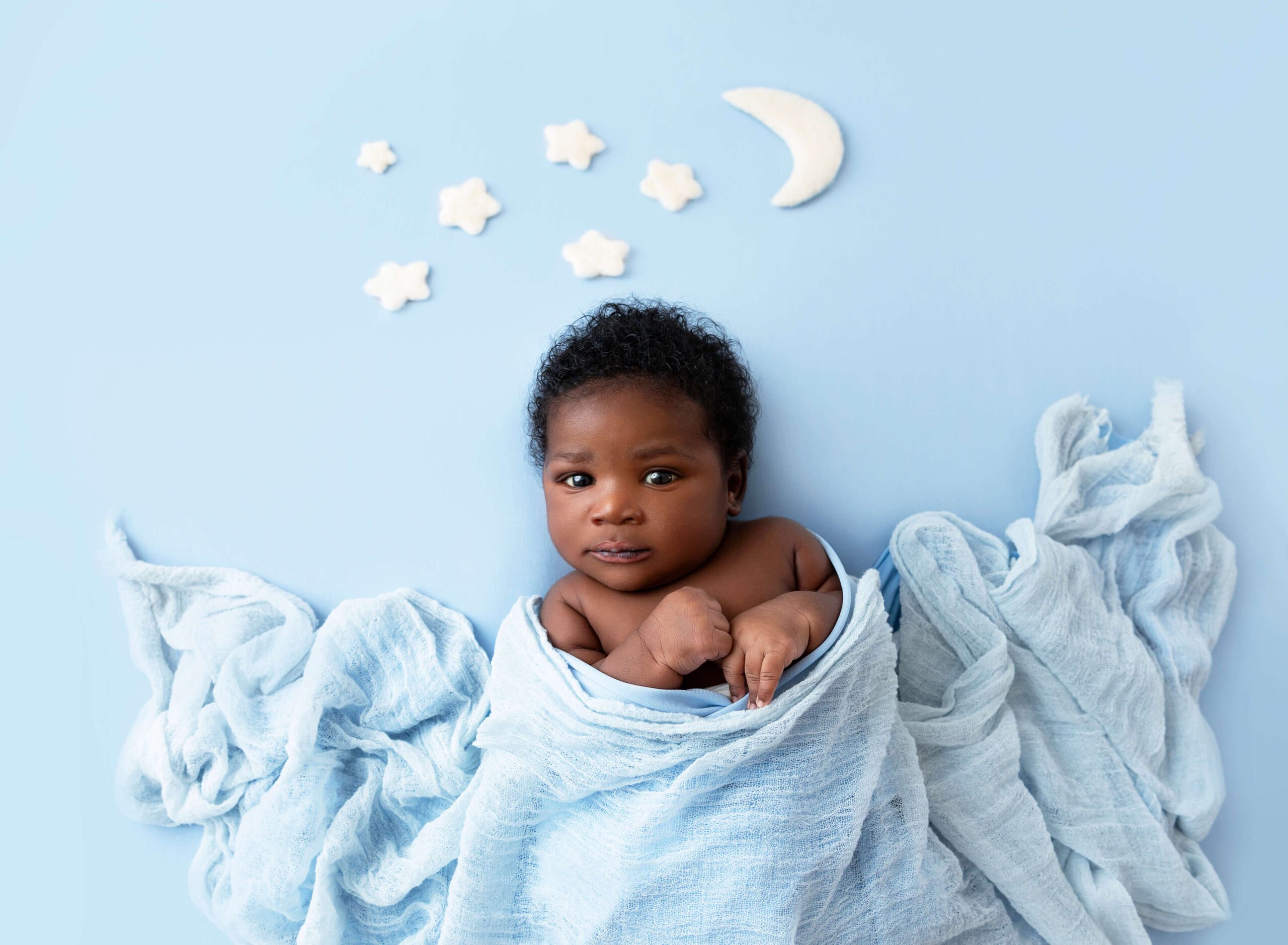 A newborn baby eyes open while laying under a blue blanket with stars and the moon after using baby shower venues in new york