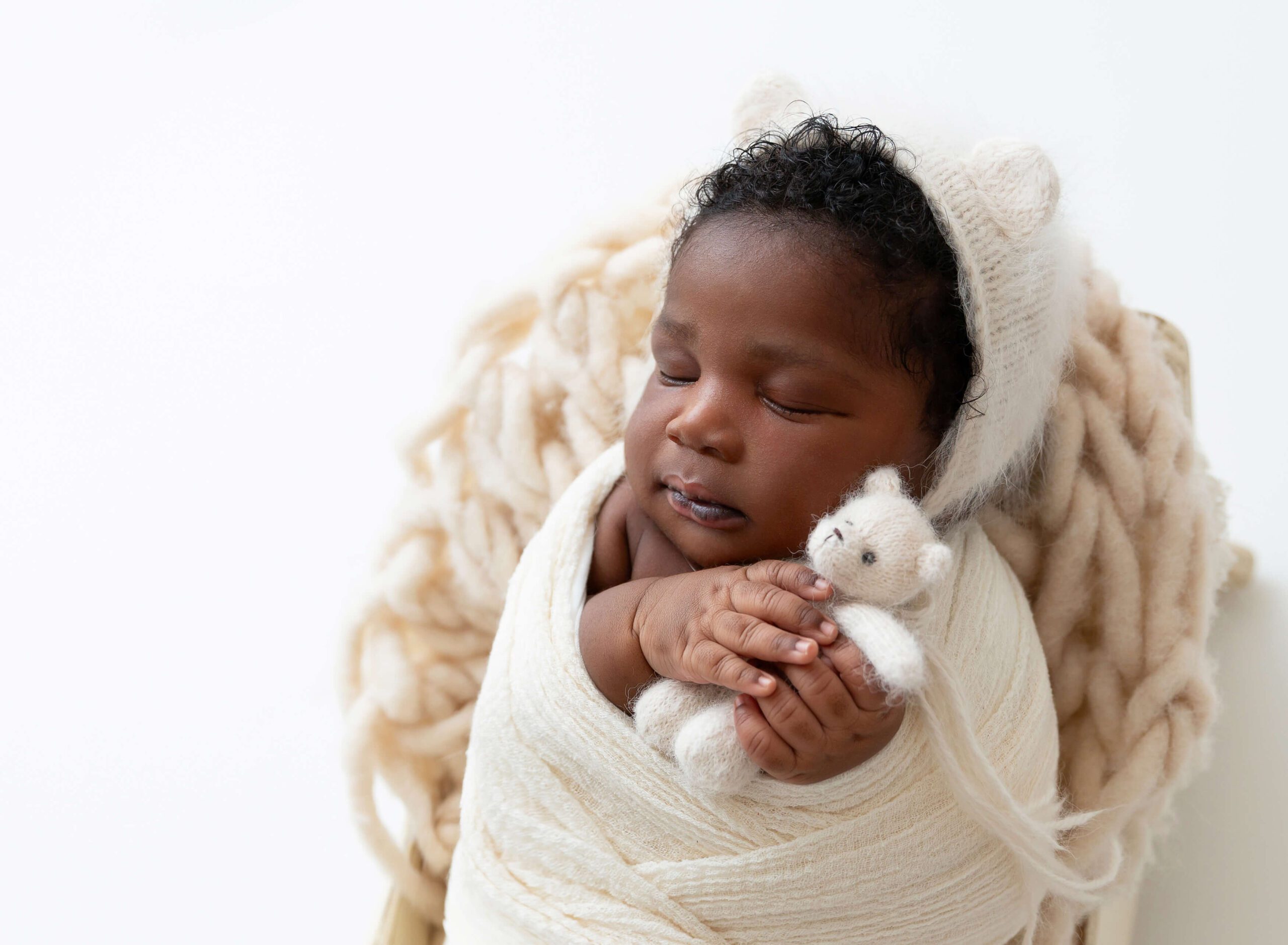 A newborn sleeps with a knit bear in a matching bonnet with ears