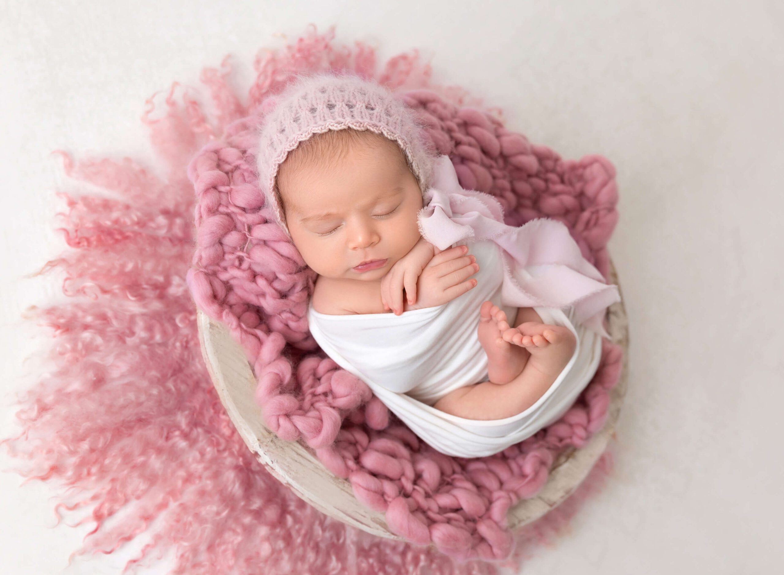 A newborn girl sleeps in a white swaddle  and pink bonnet after meeting babysitters new york