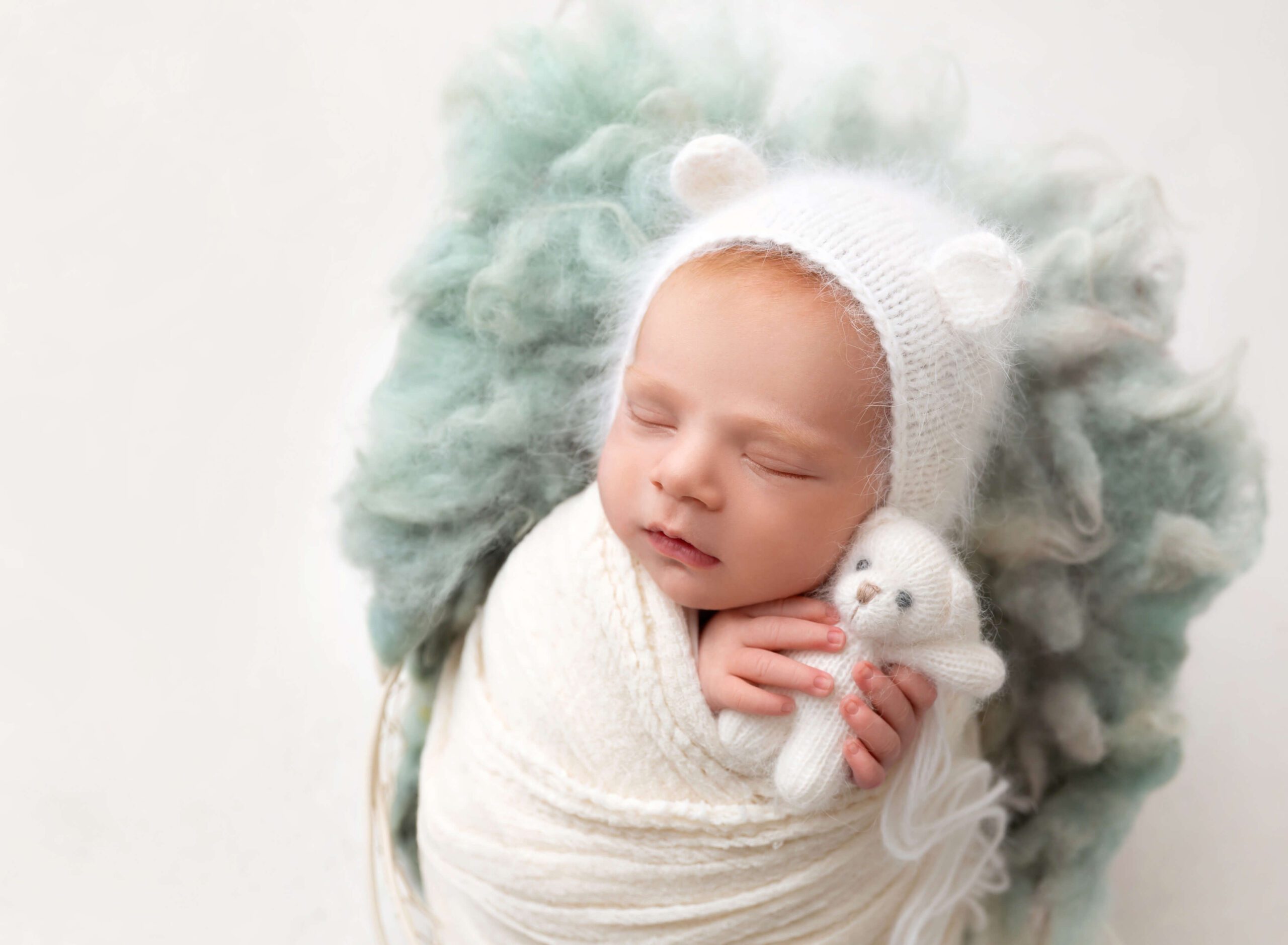 A newborn sleeps with a knit bear in a matching bonnet with ears