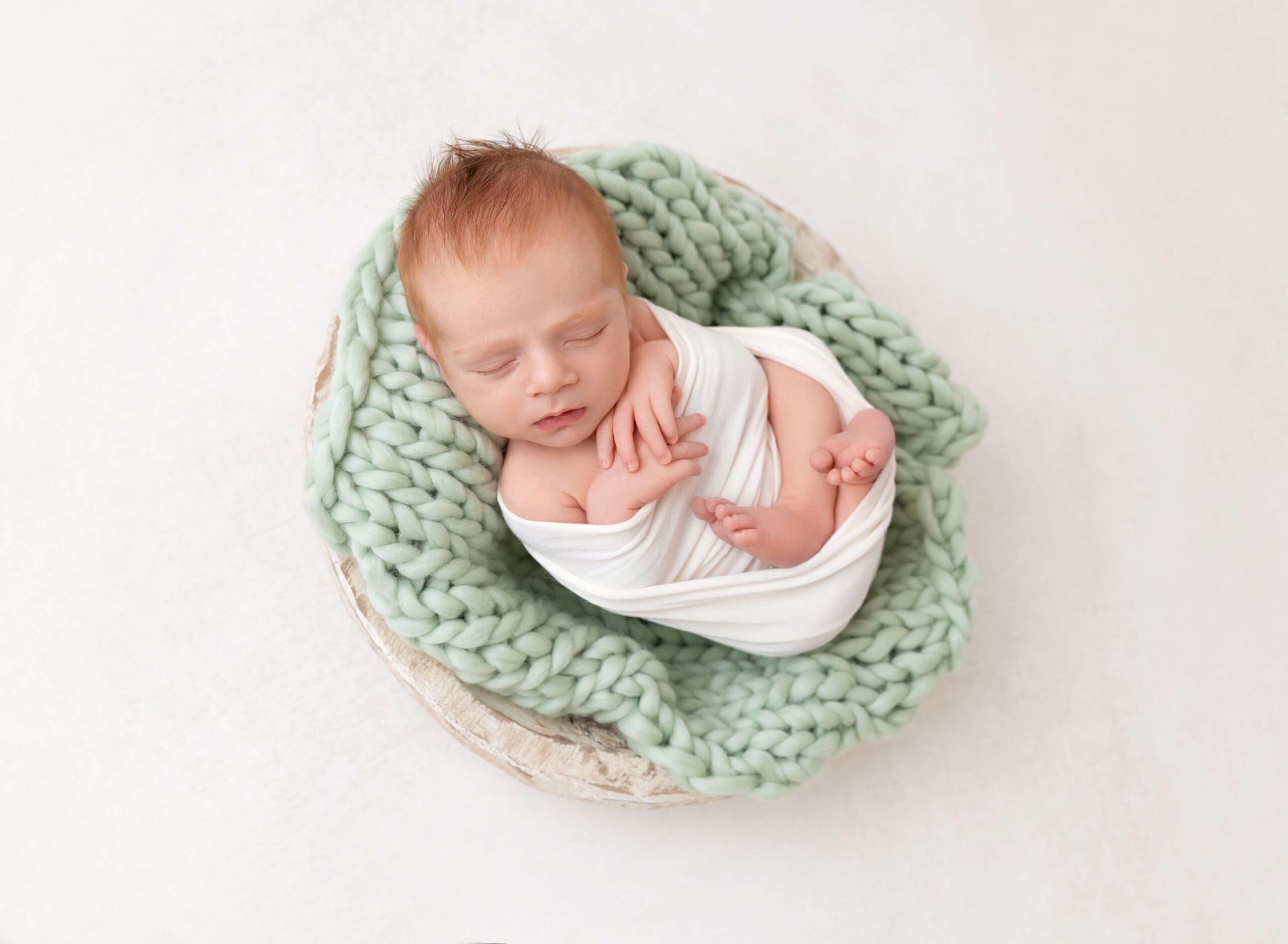 A newborn baby sleeps in a small wooden bowl on a green blanket after meeting an au pair in new york