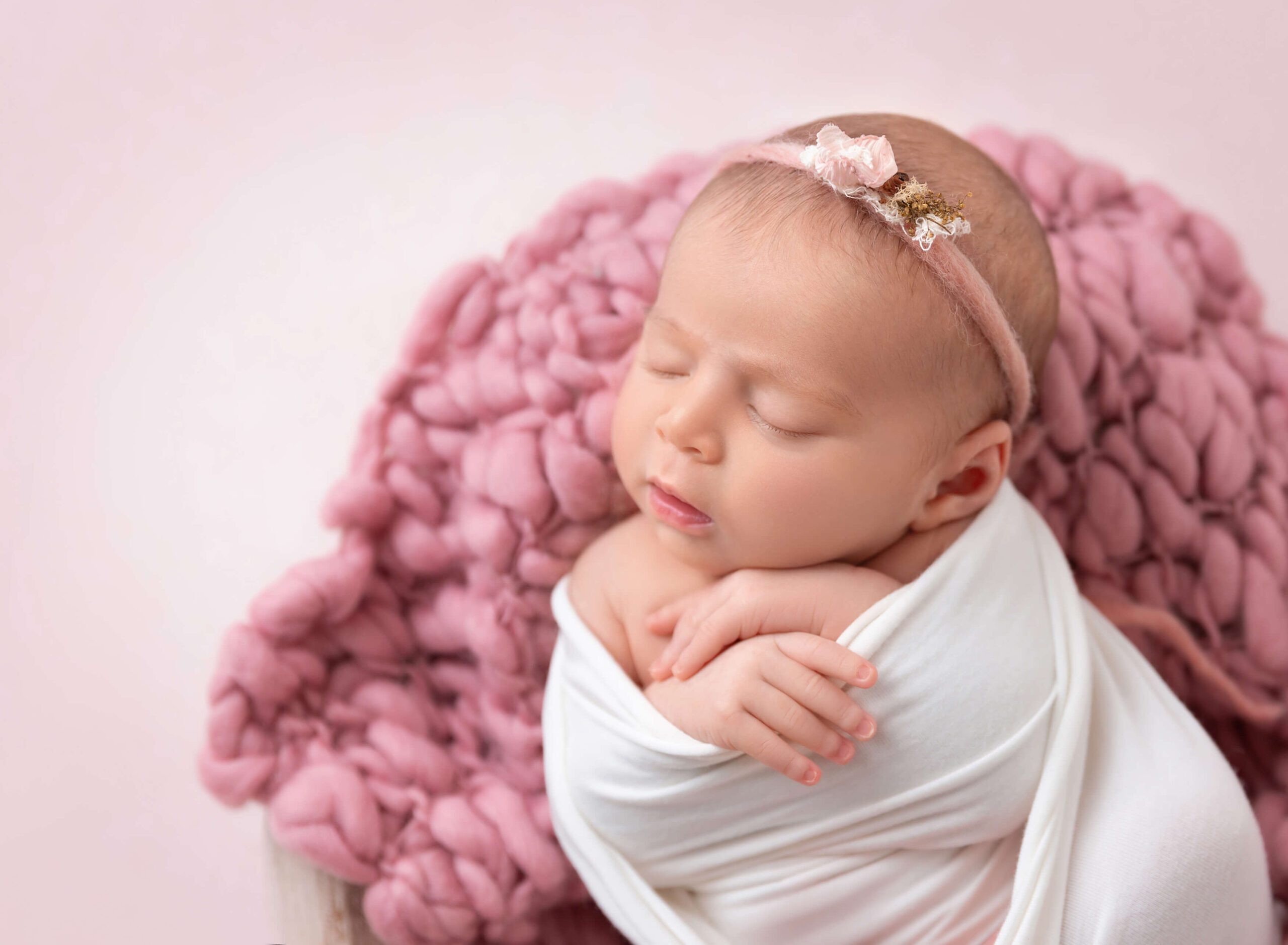 A newborn girl sleeps in a white swaddle with a floral headband after meeting babysitters new york