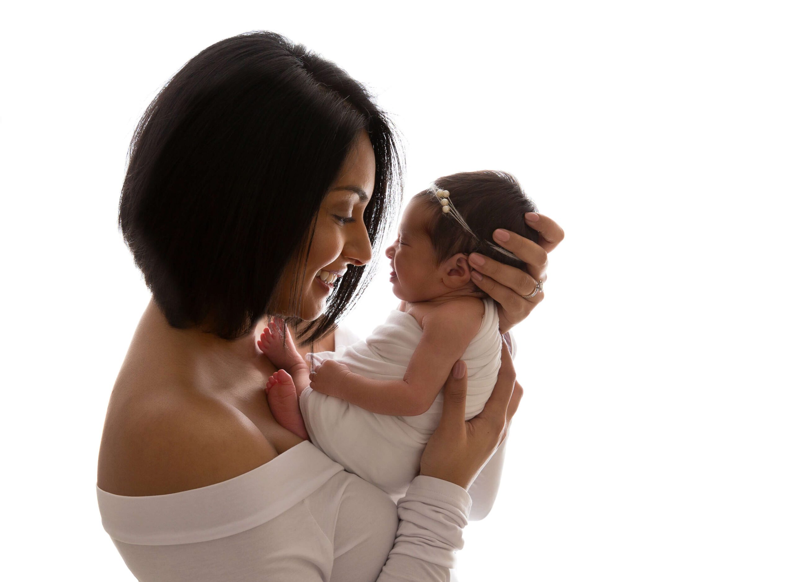 A smiling mother cradles her newborn baby both in white in a studio after using maternity stores in new york