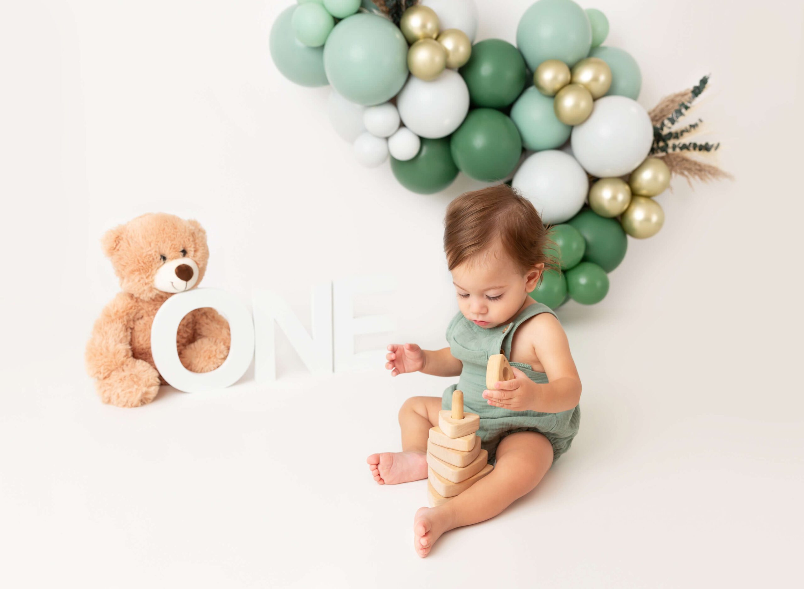 A baby in green overalls plays with wooden toy in a studio floor after some music classes for babies in nyc