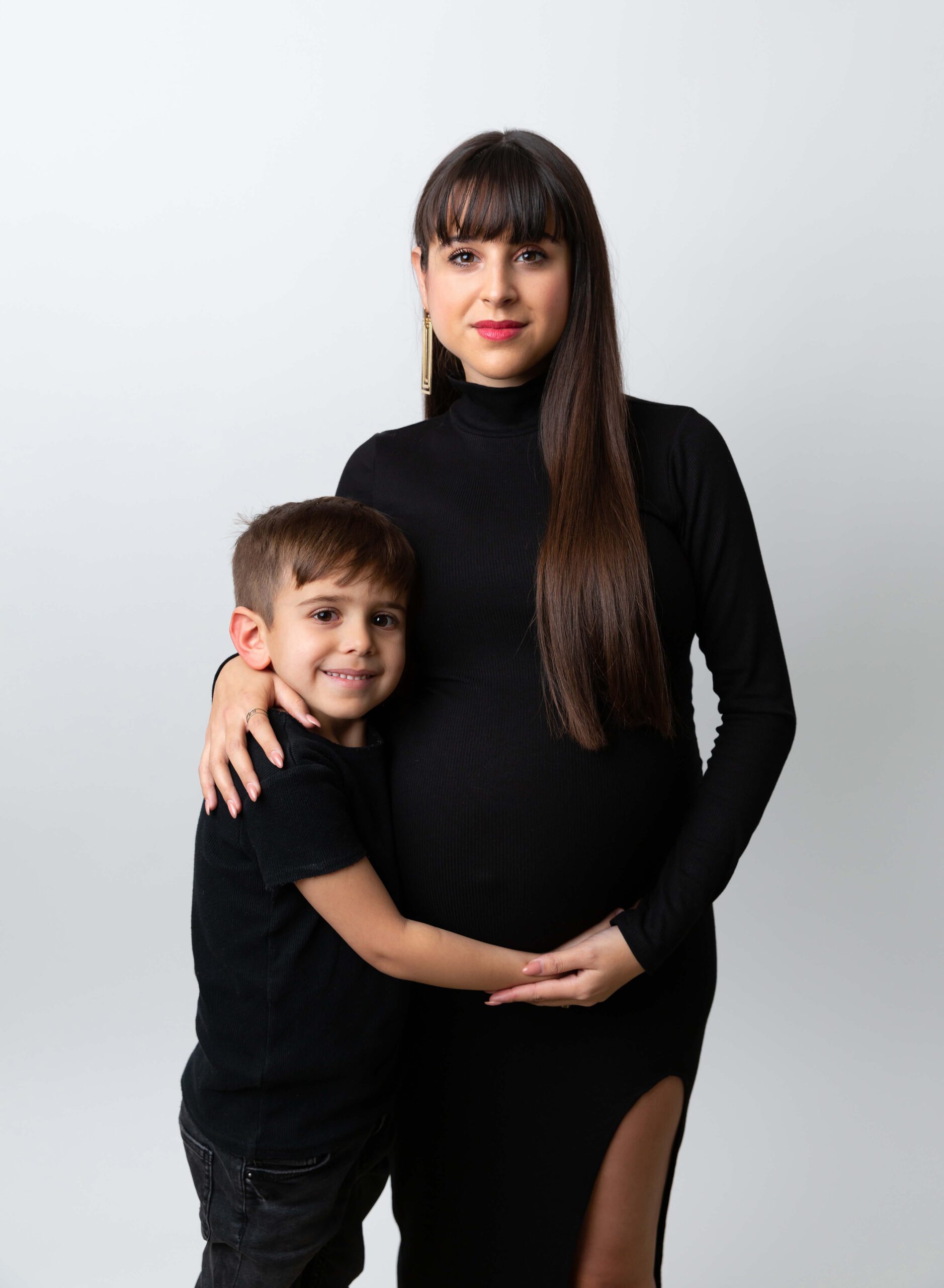 A happy toddler hugs mom's pregnant bump in black outfits in a studio before some pelvic floor therapy in new york