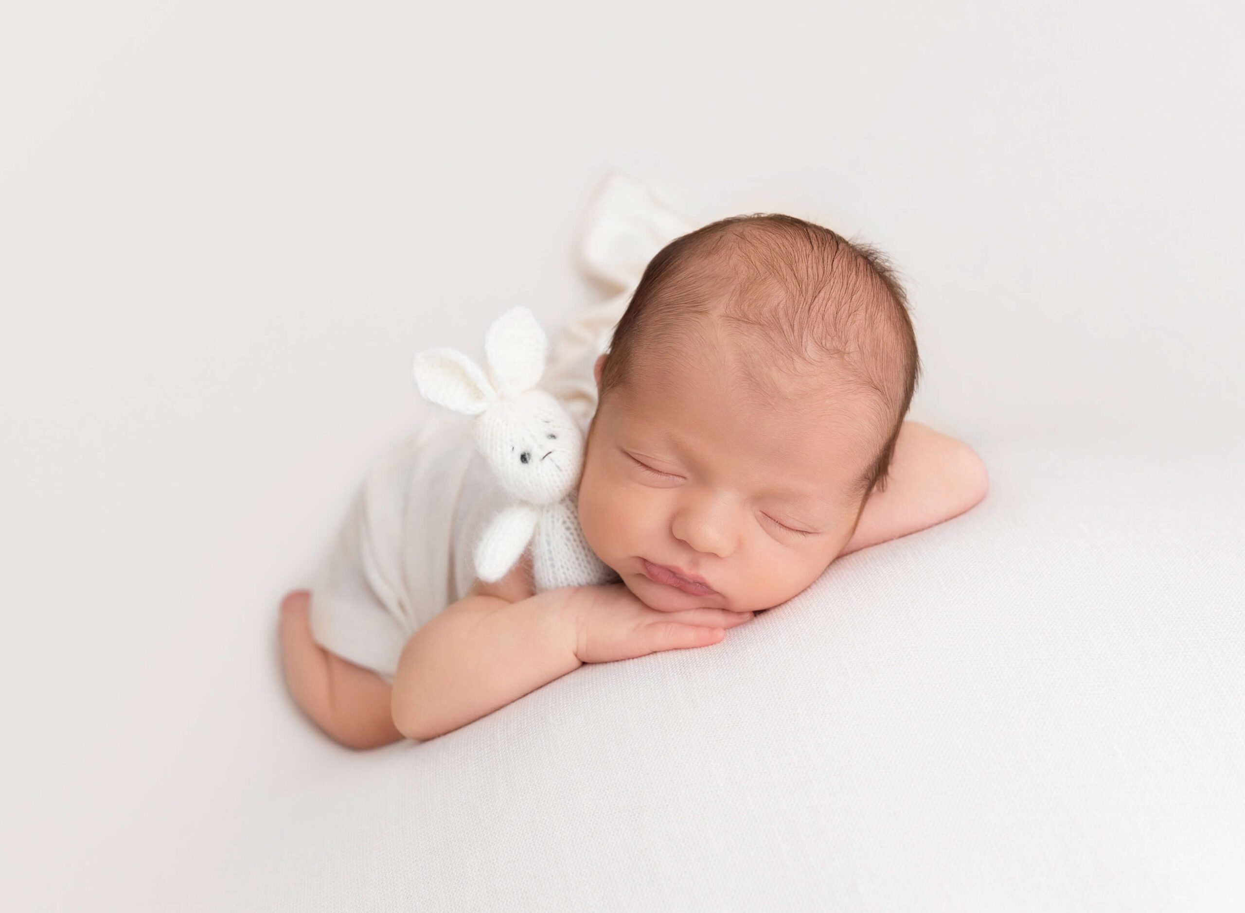 A newborn baby sleeps on its tummy with a knit bunny after mom found placenta encapsulation in new york