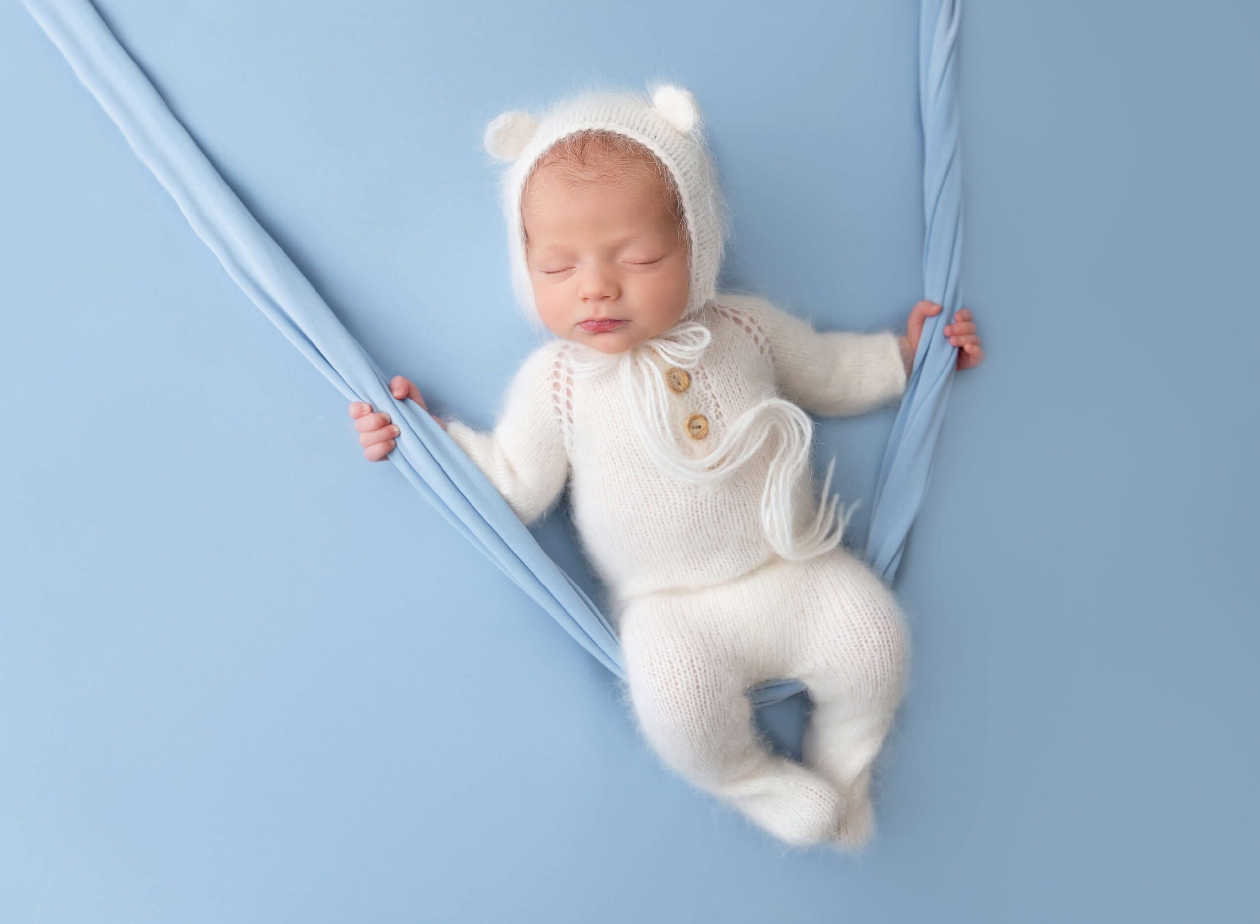 A newborn abby in a knit onesie and matching bear ear bonnet sleeps on a swing after mom found placenta encapsulation in new york