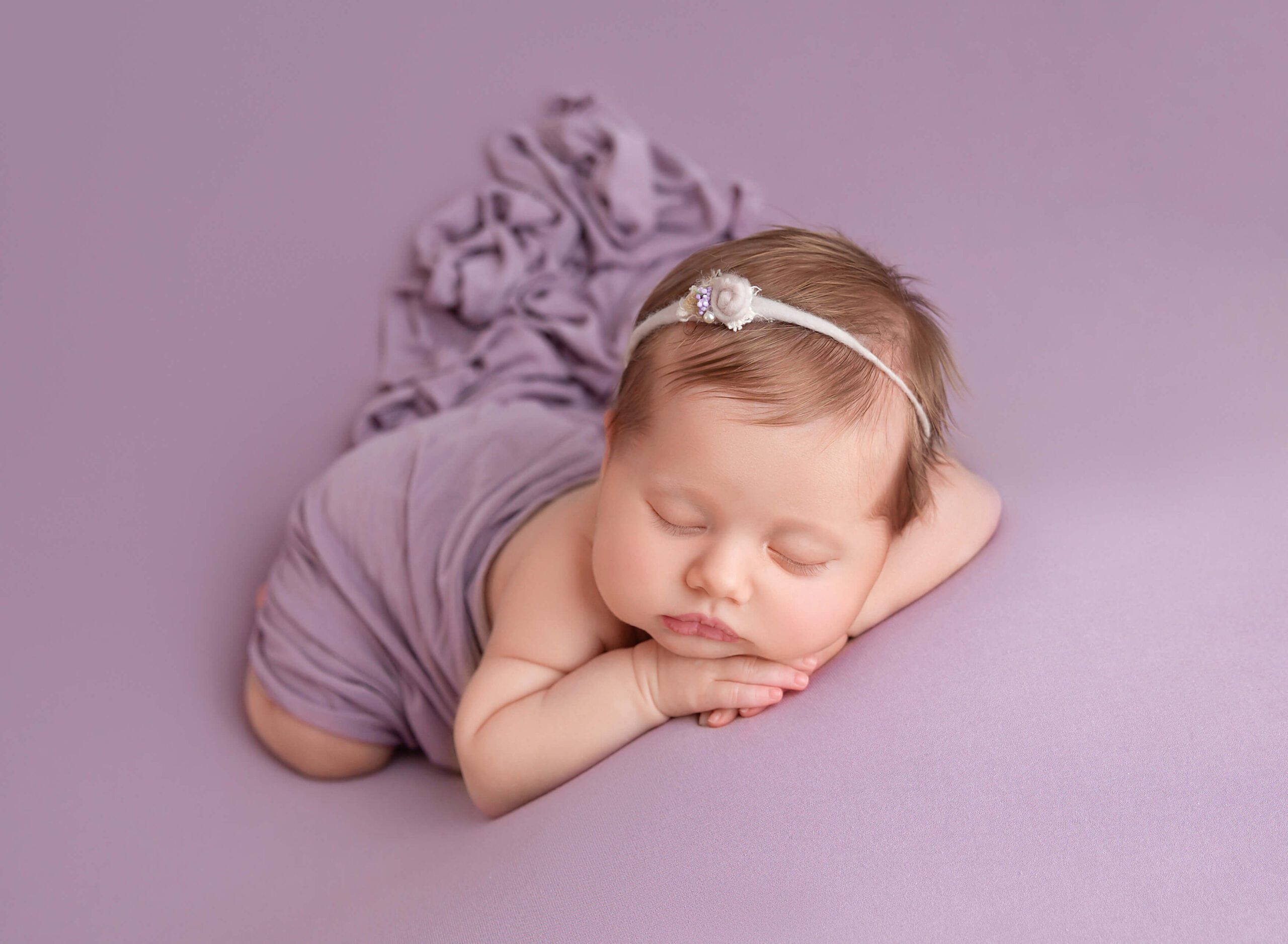 A newborn baby girl sleeps on her hands under a purple blanket thanks to TLC Midwife