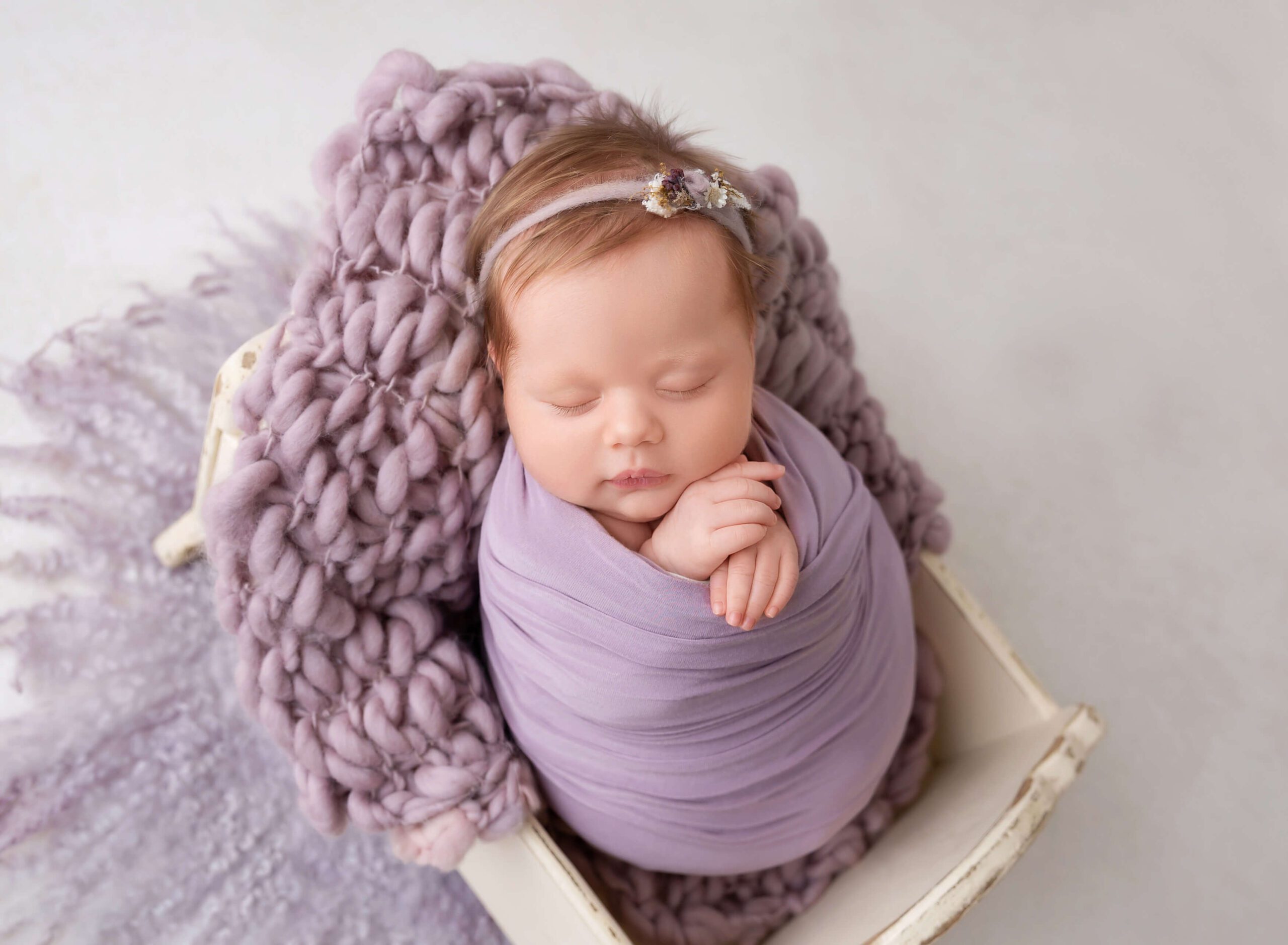 A newborn baby girl in a purple swaddle sleeps in a tiny wooden crib thanks to TLC Midwife