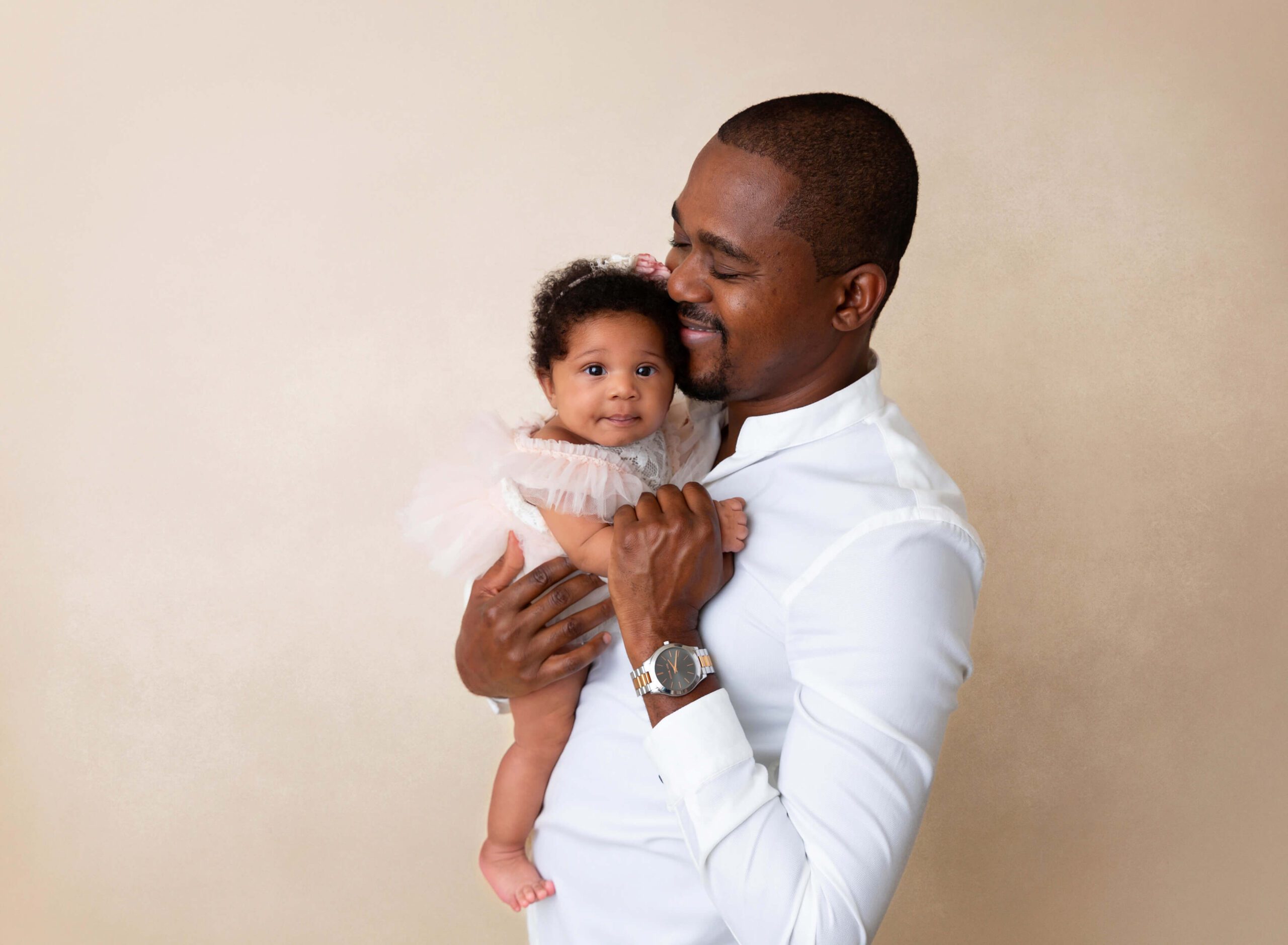 A happy dad snuggles his newborn girl in a studio after his babymoon in new york