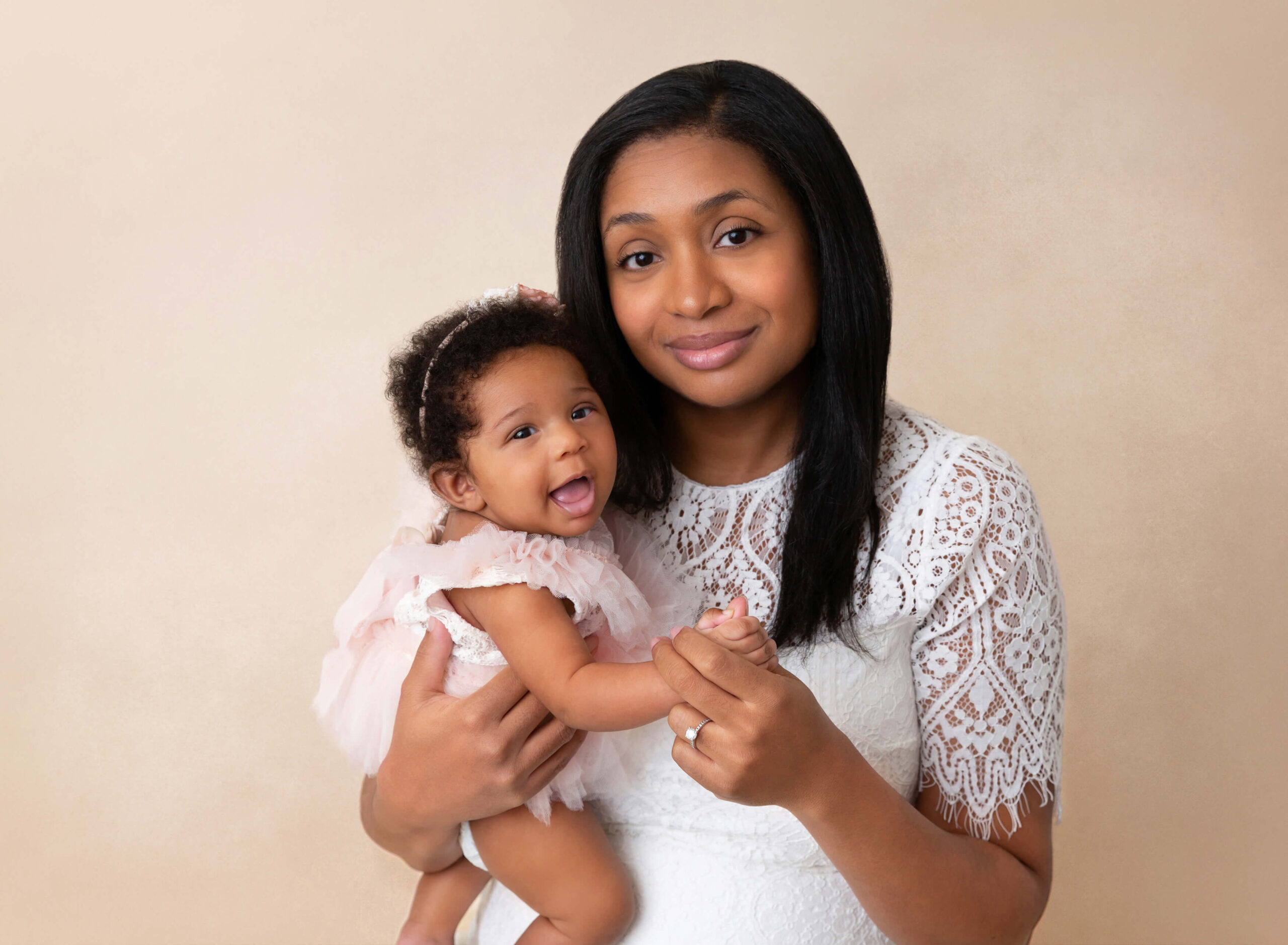 A happy baby girl laughs while sitting in mom's arms in a studio after mom's babymoon in new york