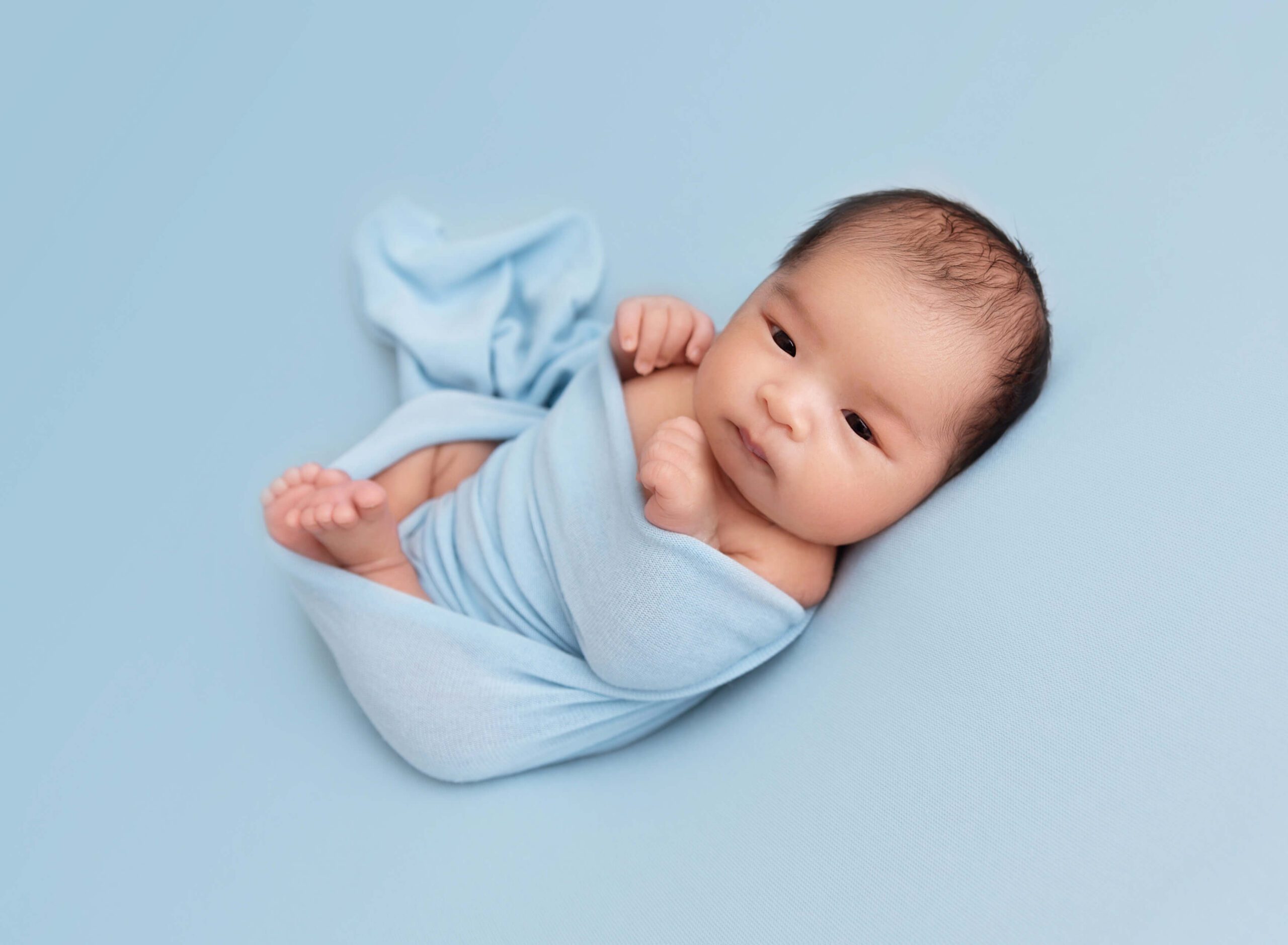 A newborn baby lays on its back in a blue swaddle after a water birth in new york