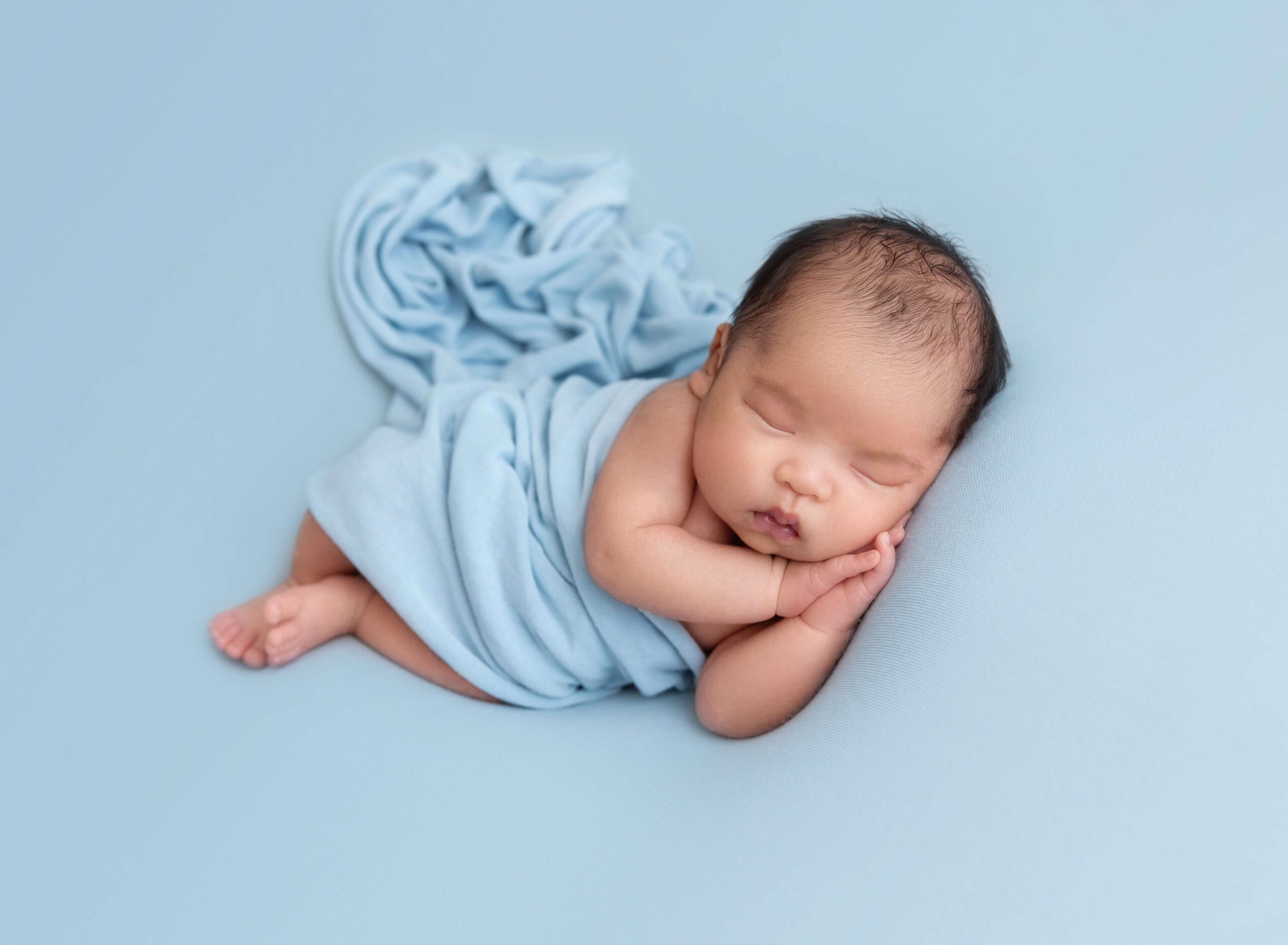 A newborn baby sleeps on its side under a blue blanket on matching bed after a water birth in new york