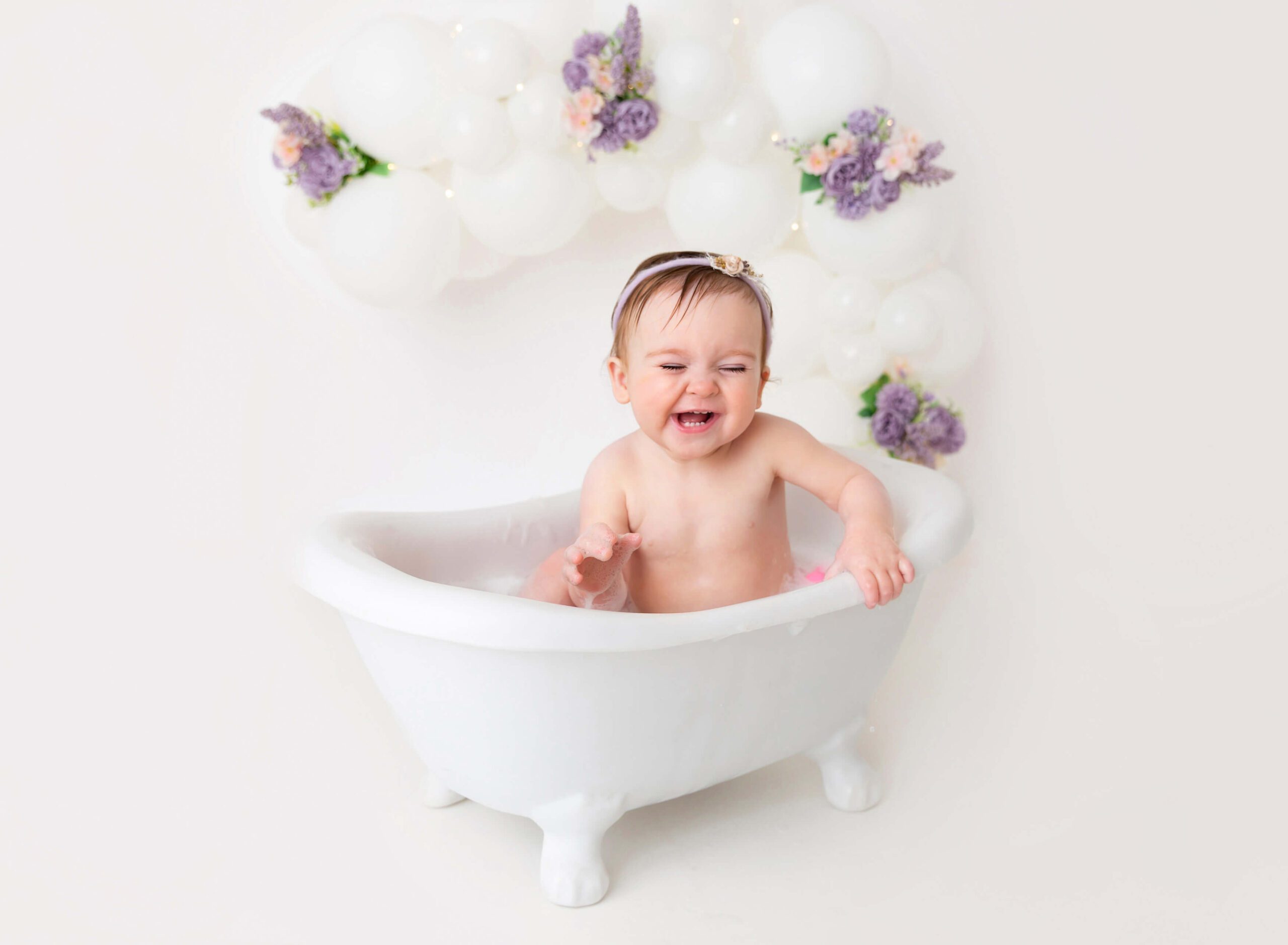 A giggling baby girl plays in a bathtub in a studio