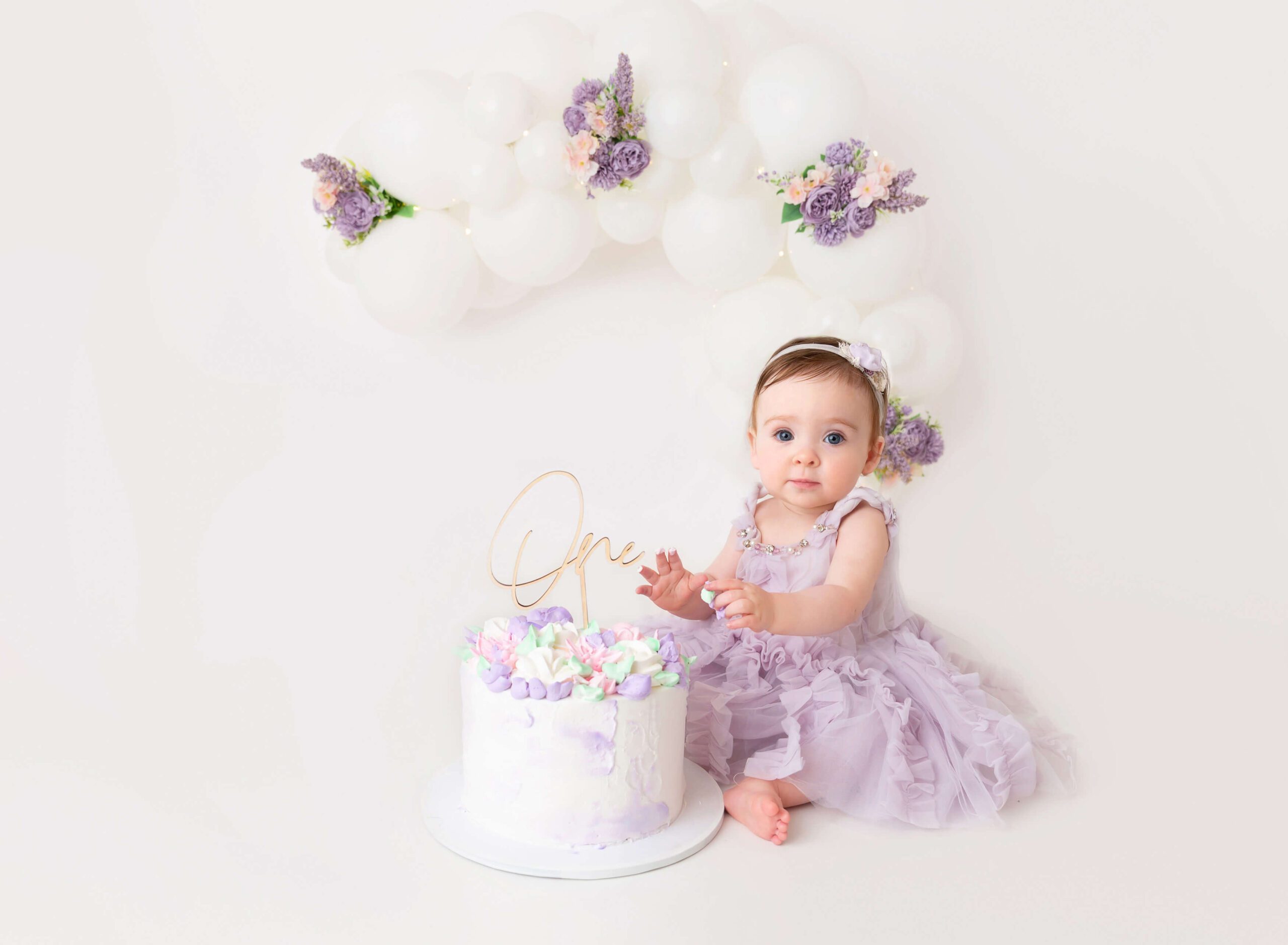 A baby girl smashes her first birthday cake in a studio in a purple dress thanks to birth matters nyc