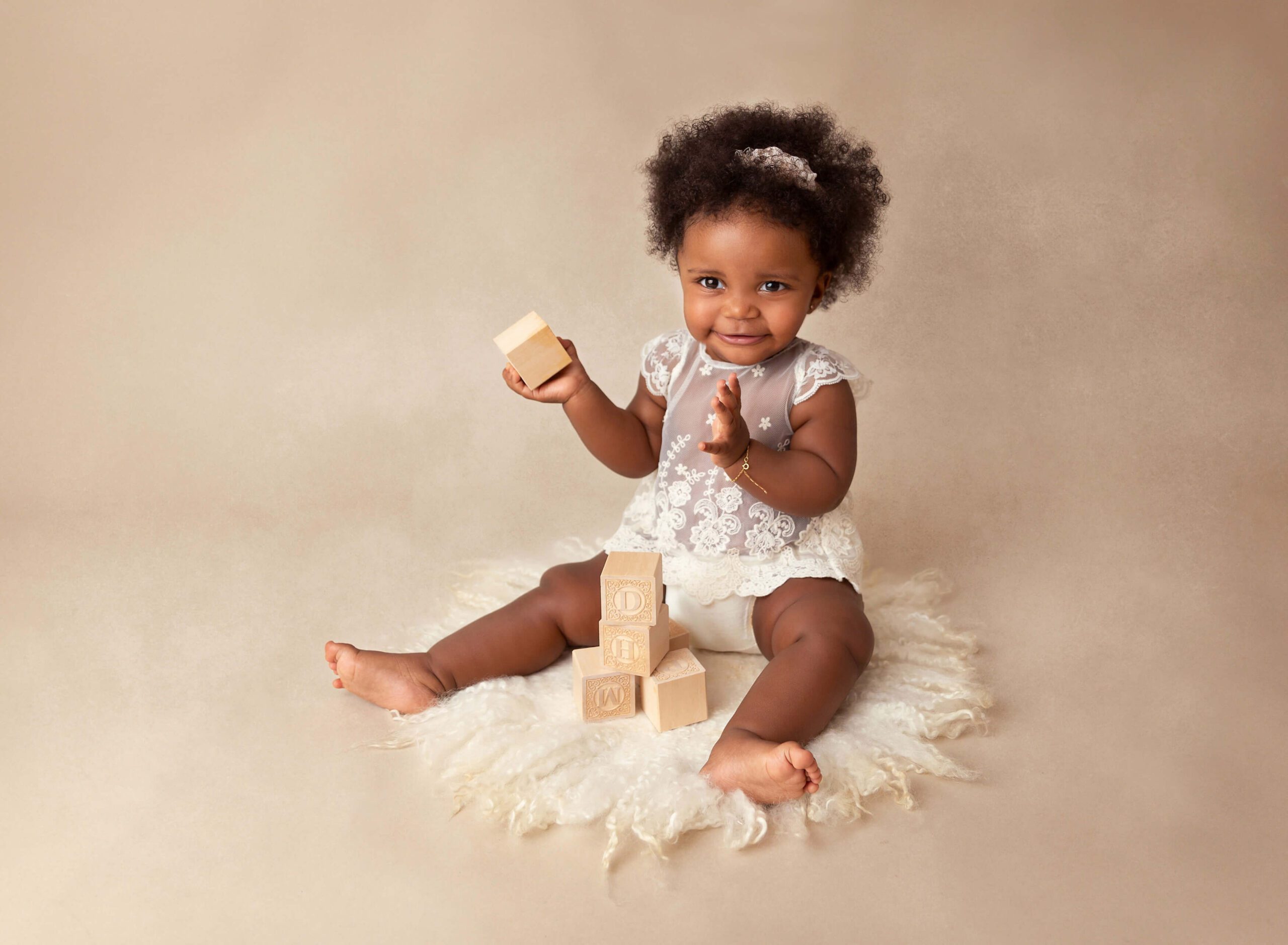 A baby girl in a white lace blouse sits in a studio playing with wood blocks after some Baby Classes In NYC