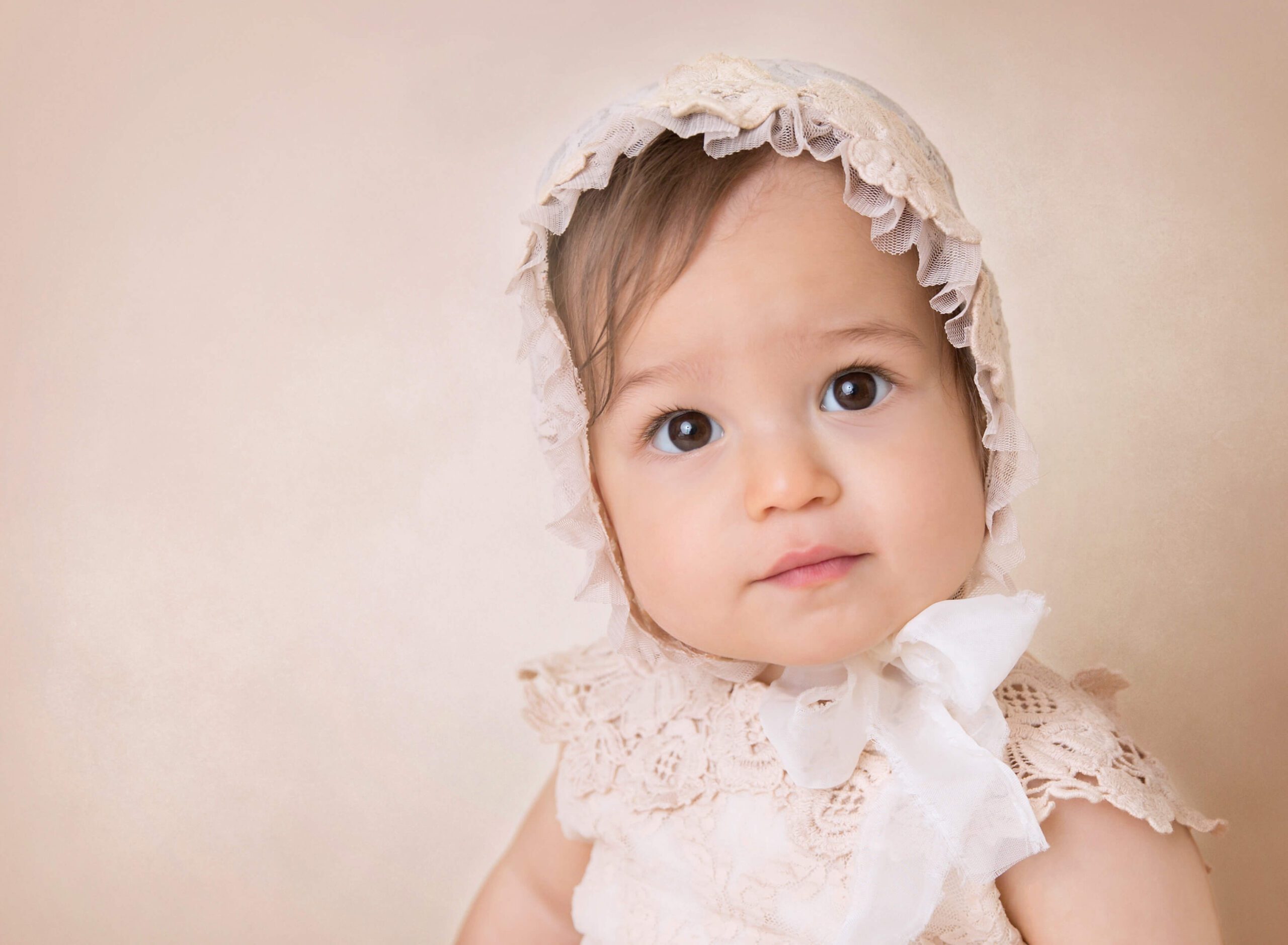An infant girl smiles in a lace bonnet and dress in a studio after some Baby Yoga In NYC