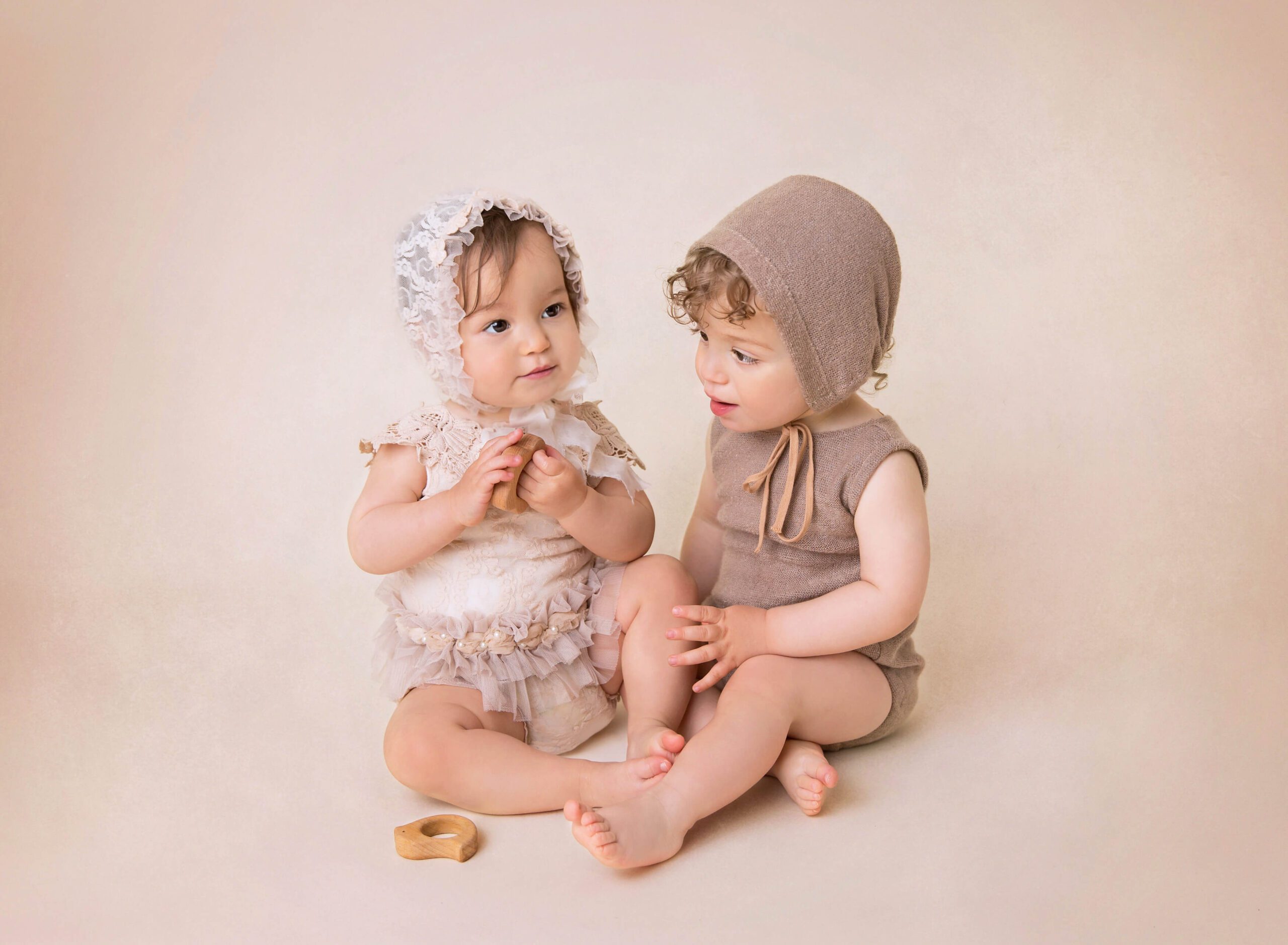 Twin infants sit on a studio floor playing with wooden toys after visiting Daycares In NYC