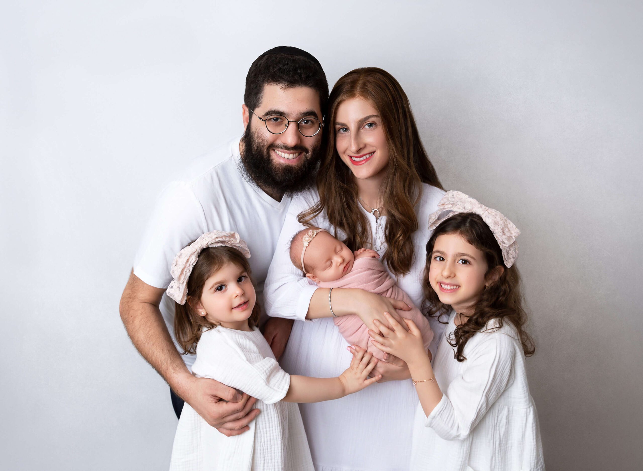 Toddler sisters stand with mom and dad all with hands on sleeping newborn after visiting Everything But The Baby in Brooklyn