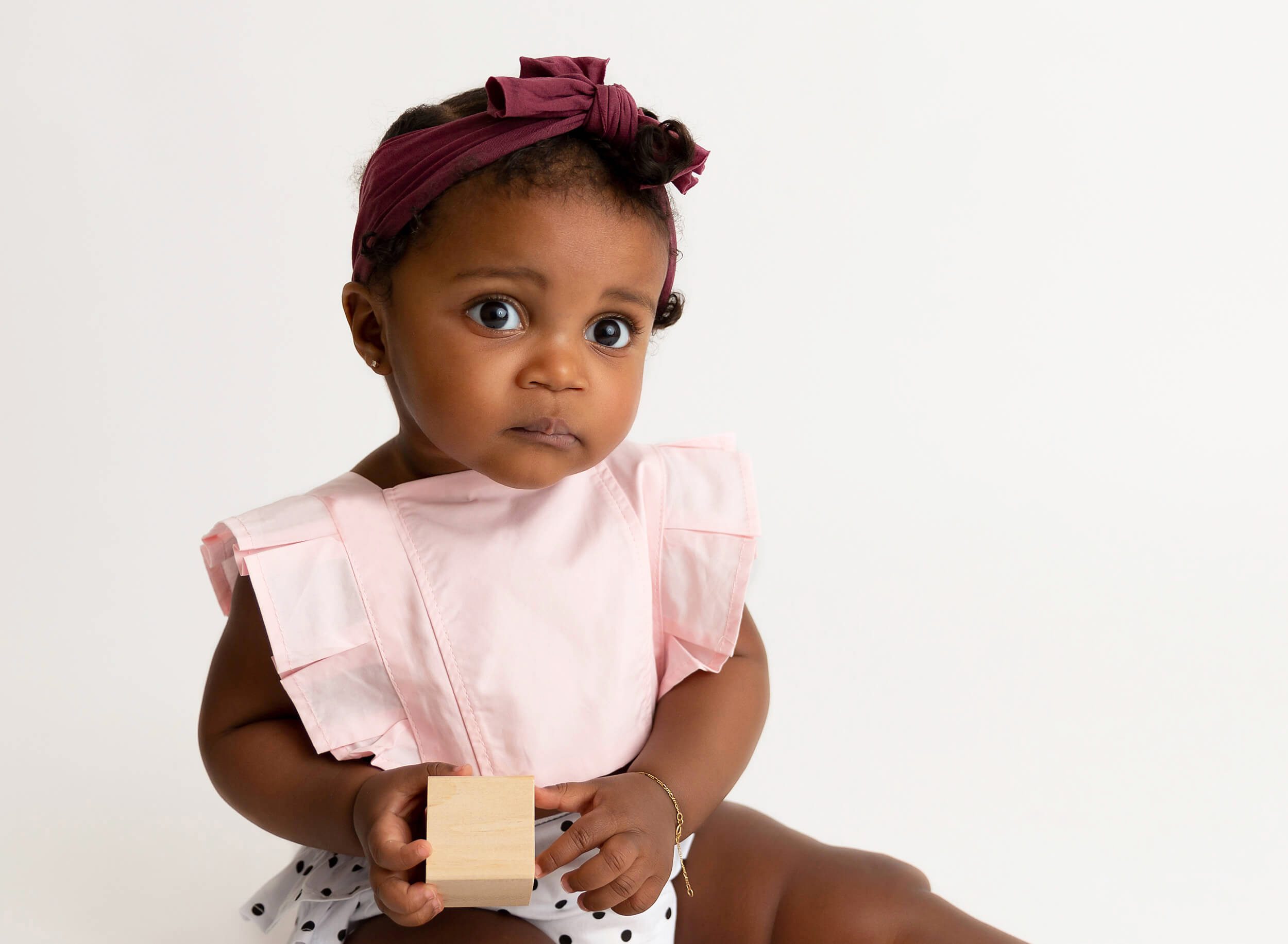 A baby girl sits in a polka dot dress and pink top playing with wooden blocks in a studio after visiting Pediatric Chiropractors In NYC