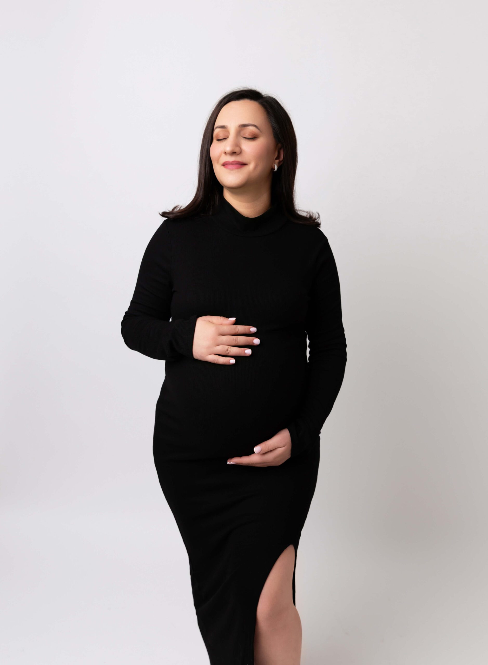 A mother to be rests her hands on her bump in a black bodysuit dress after visiting Prenatal Chiropractors In NYC